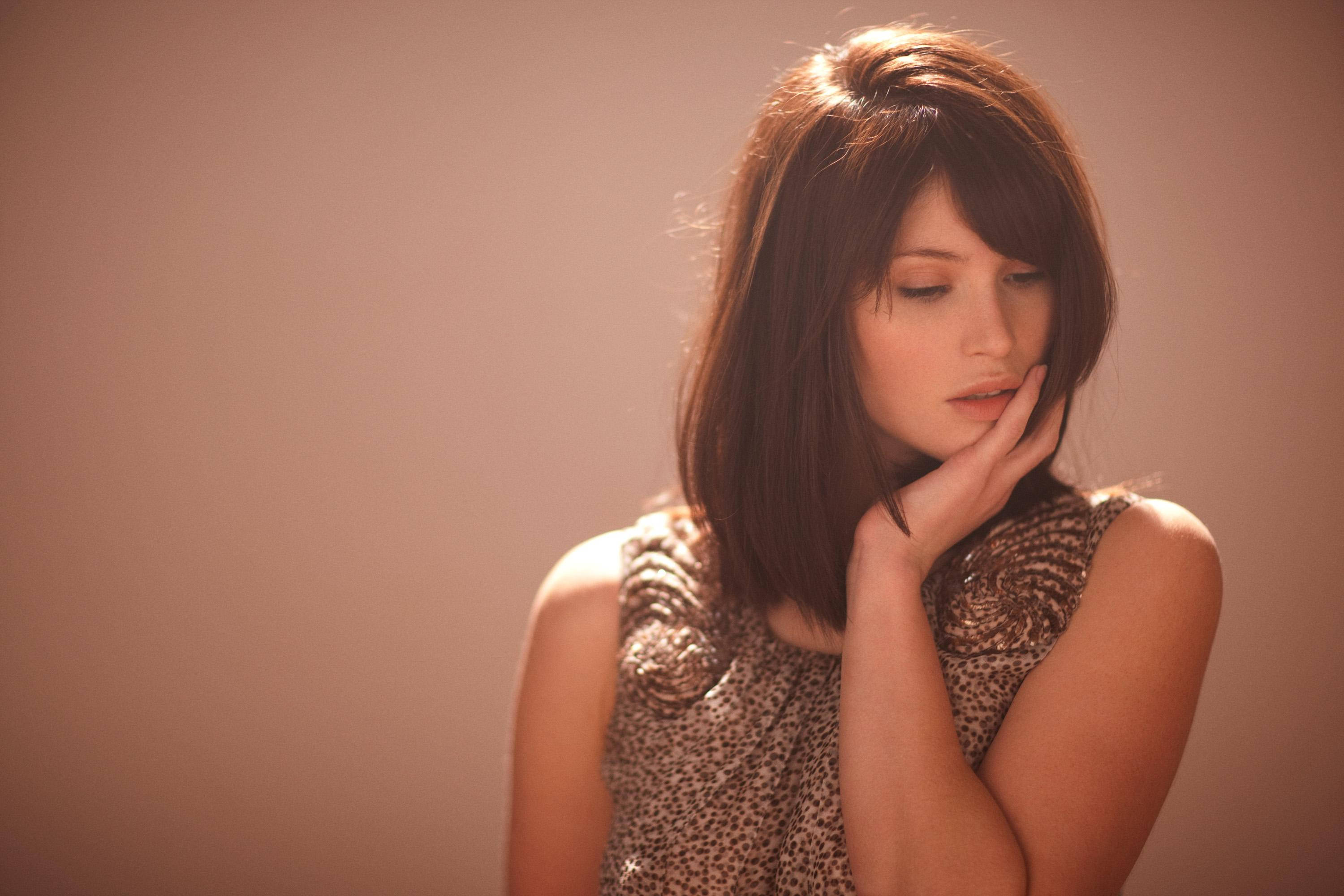 Gemma Arterton 桌布 壁紙 — 一位棕色頭髮的女性將下巴靠在手上，背景是柔和的棕色，閉著眼睛靜靜沉思。