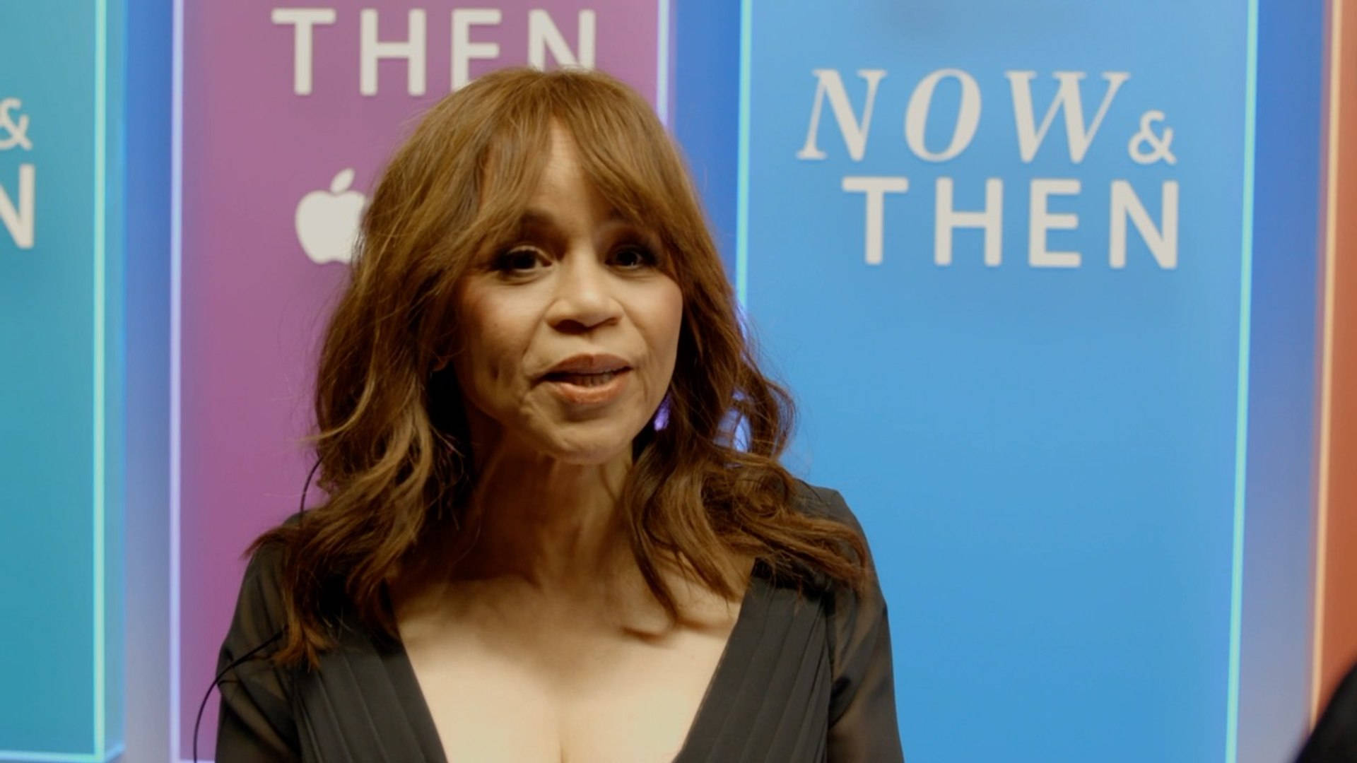 Celebrity 桌布 壁紙 — 一位棕色頭髮的女性站在色彩繽紛的「NOW & THEN」Apple 活動背景前，微微一笑。