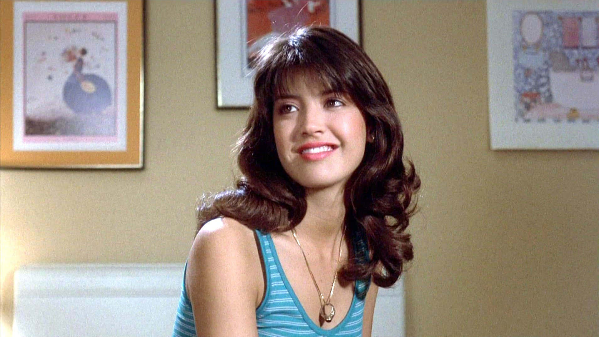 Phoebe Cates 桌布 壁紙 — 一位棕色頭髮的年輕女性在陽光充足的房間裡溫暖地微笑，房間內有米色牆壁和裱框藝術品。