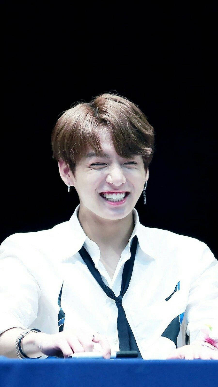 Jungkook 桌布 壁紙 — 一位棕色頭髮的年輕男子在黑色背景前穿著白襯衫和黑色領帶，開懷大笑。