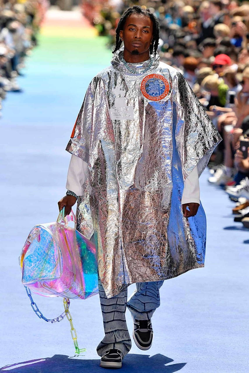 Carti 桌布 壁紙 — 一位模特兒在明亮的日光下，穿著閃亮的銀色斗篷，拿著全息袋，走在藍色天橋上。