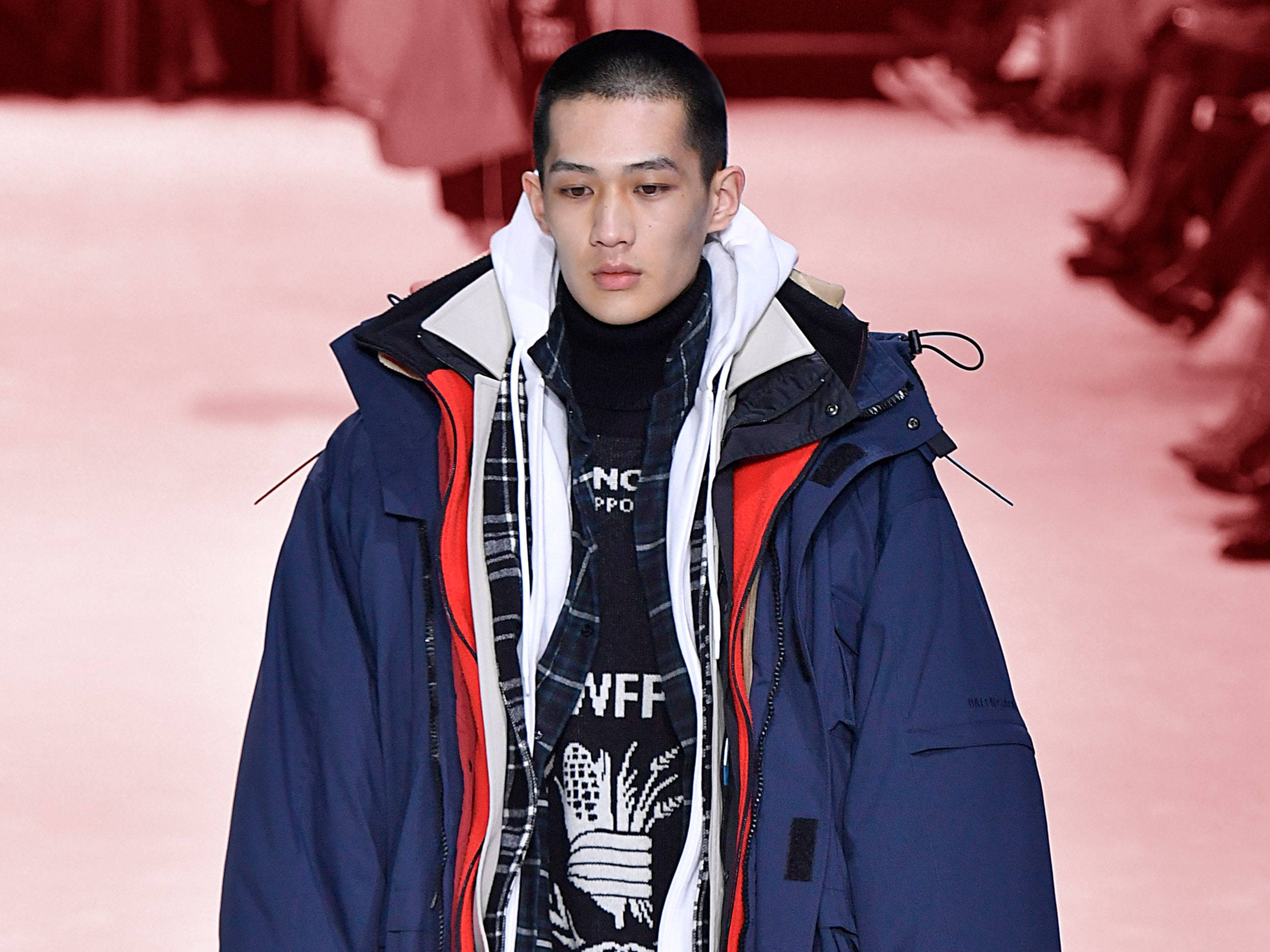 Balenciaga 桌布 壁紙 — 一位模特兒在時裝天橋上走秀，穿著分層的冬季服裝，包括一件海軍藍色外套配紅色內裡和圖案高領毛衣。