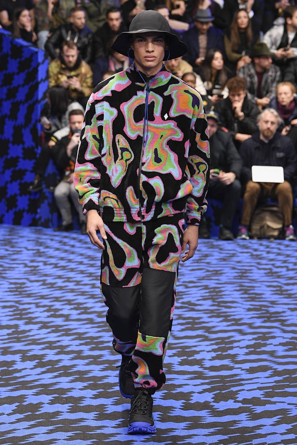 Fashion Model 桌布 壁紙 — 一位模特兒穿著充滿活力的迷幻圖案運動服和黑色漁夫帽走在伸展台上。