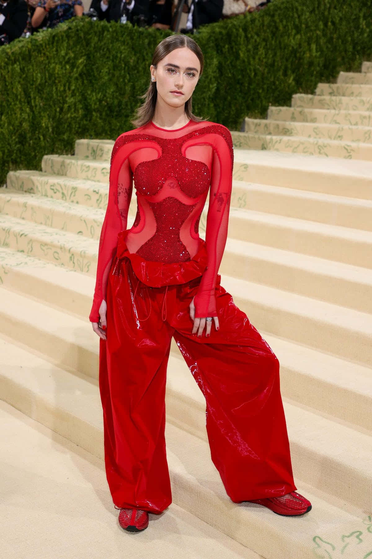 Met Gala 2021 桌布 壁紙 — 一位模特兒穿著大膽的紅色亮片連體衣和寬鬆天鵝絨長褲，在高級時尚活動的華麗樓梯上擺姿勢。