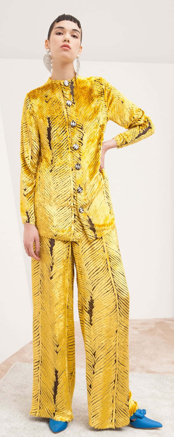Yellow Fashion 桌布 壁紙 — 一位模特兒穿著大膽的黃色天鵝絨西裝，帶有黑色羽毛圖案，在簡約的白色背景前自信地擺姿勢。