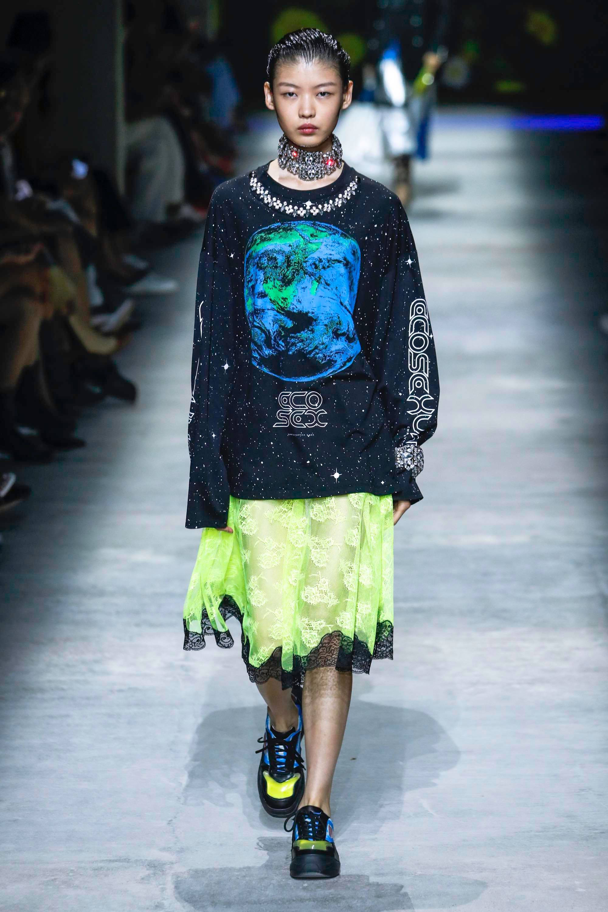Clothes 桌布 壁紙 — 一位模特兒穿著帶有藍綠色星球圖案的黑色星星運動衫和螢光黃色蕾絲裙走在天橋上。