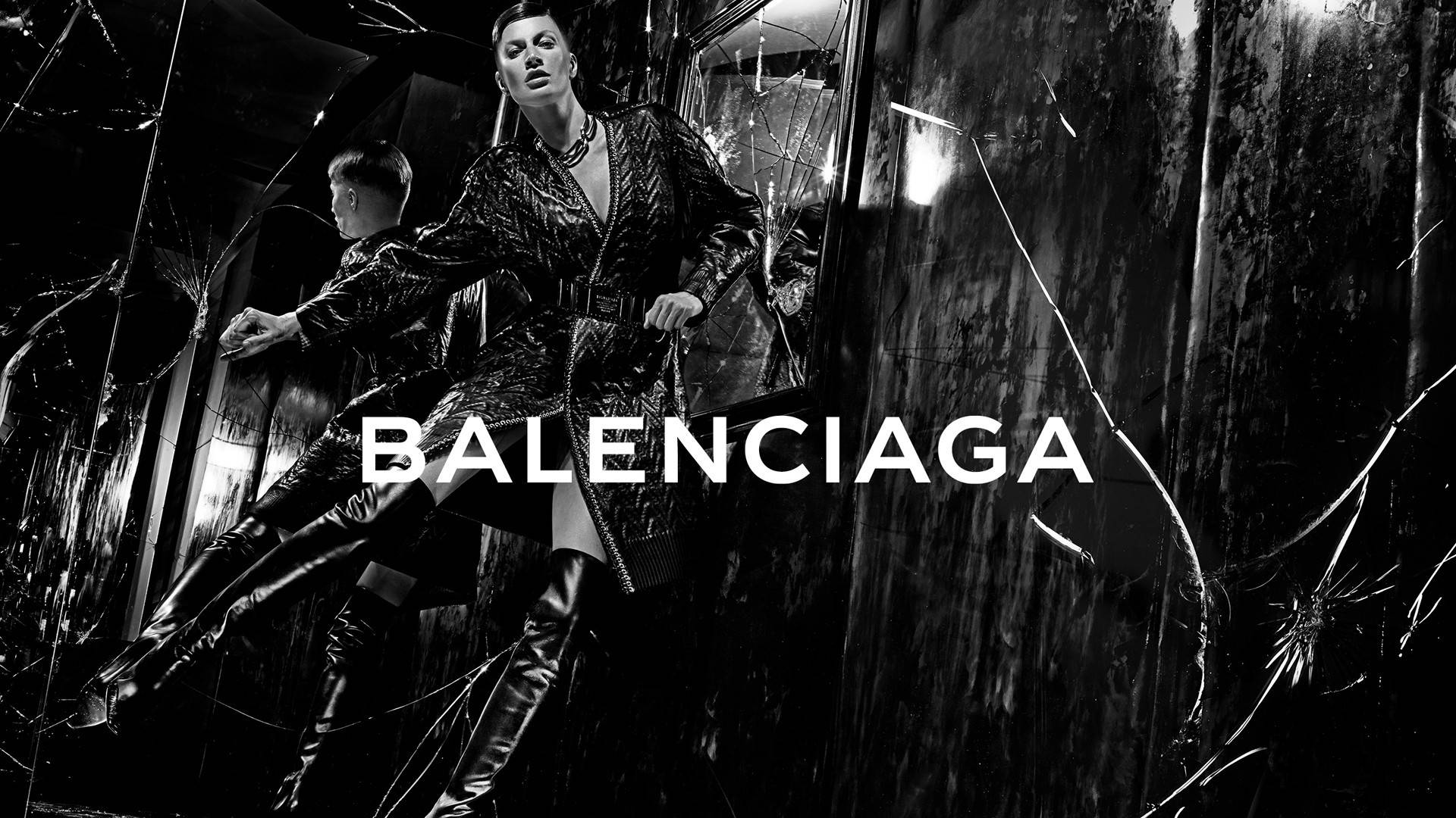 Balenciaga 桌布 壁紙 — 一位模特兒穿著質感外套和過膝靴，在破碎玻璃背景前，於高對比黑白Balenciaga廣告中戲劇性地擺姿勢。