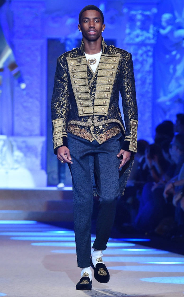 Runway 桌布 壁紙 — 一位模特兒穿著飾有精緻刺繡的華麗黑金軍裝風格外套和相配的天鵝絨拖鞋走在伸展台上。