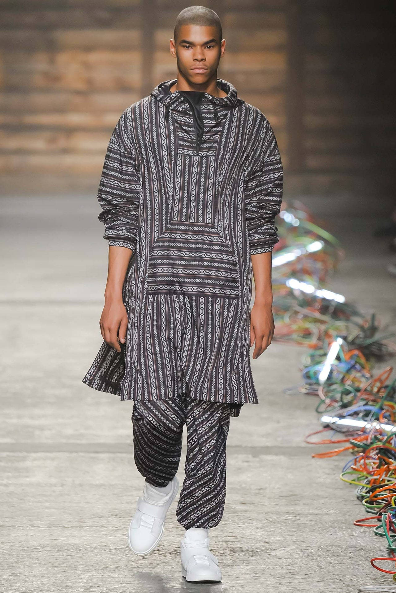 Fashion Model 桌布 壁紙 — 一位模特兒穿著黑白幾何圖案連帽服裝和白色運動鞋走在伸展台上。