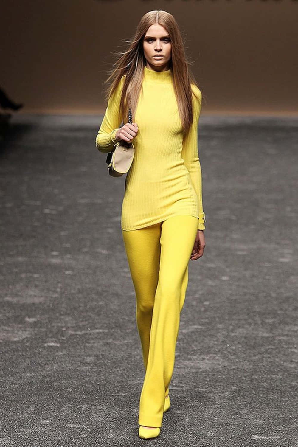Yellow Fashion 桌布 壁紙 — 一位模特兒自信地走在伸展台上，身穿大膽的黃色羅紋高領毛衣和相配的寬腿褲。