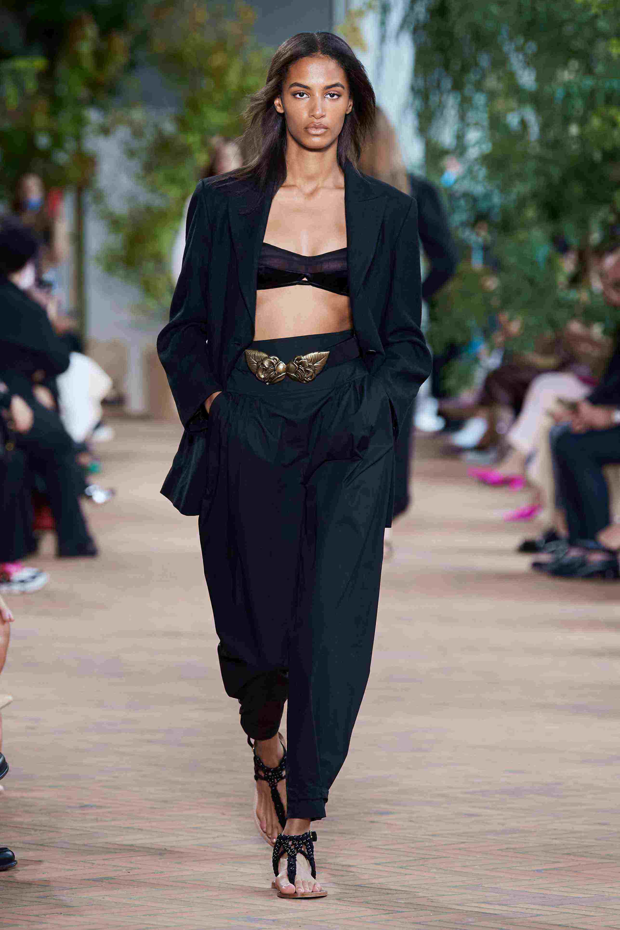 Minimalist Fashion 桌布 壁紙 — 一位模特兒自信地走在伸展台上，身穿黑色西裝外套短版上衣和寬褲，搭配金色腰帶點綴。
