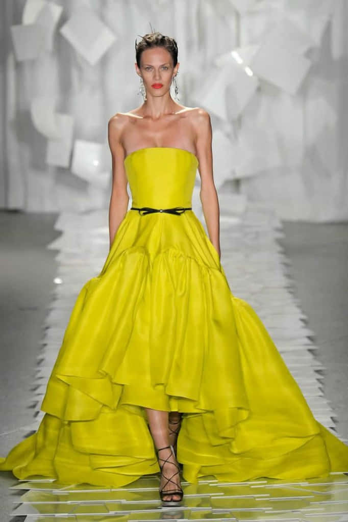 Yellow Fashion 桌布 壁紙 — 一位模特兒自信地走在伸展台上，身穿鮮黃色無肩帶長裙，搭配黑色腰帶和高低裙襬。