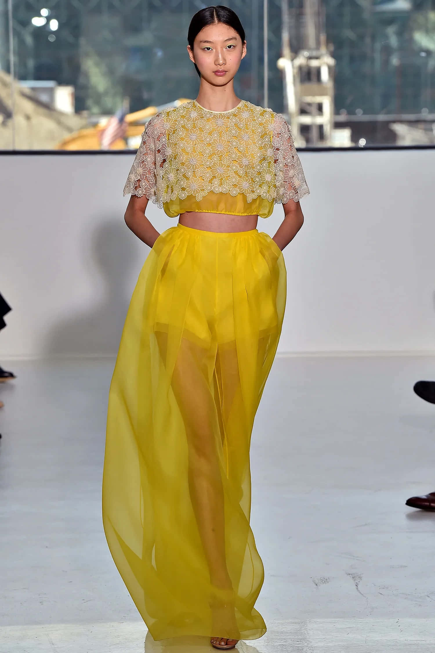 Yellow Fashion 桌布 壁紙 — 一位模特兒自信地走在伸展台上，身穿鮮黃色蕾絲短版上衣和飄逸的薄紗裙。