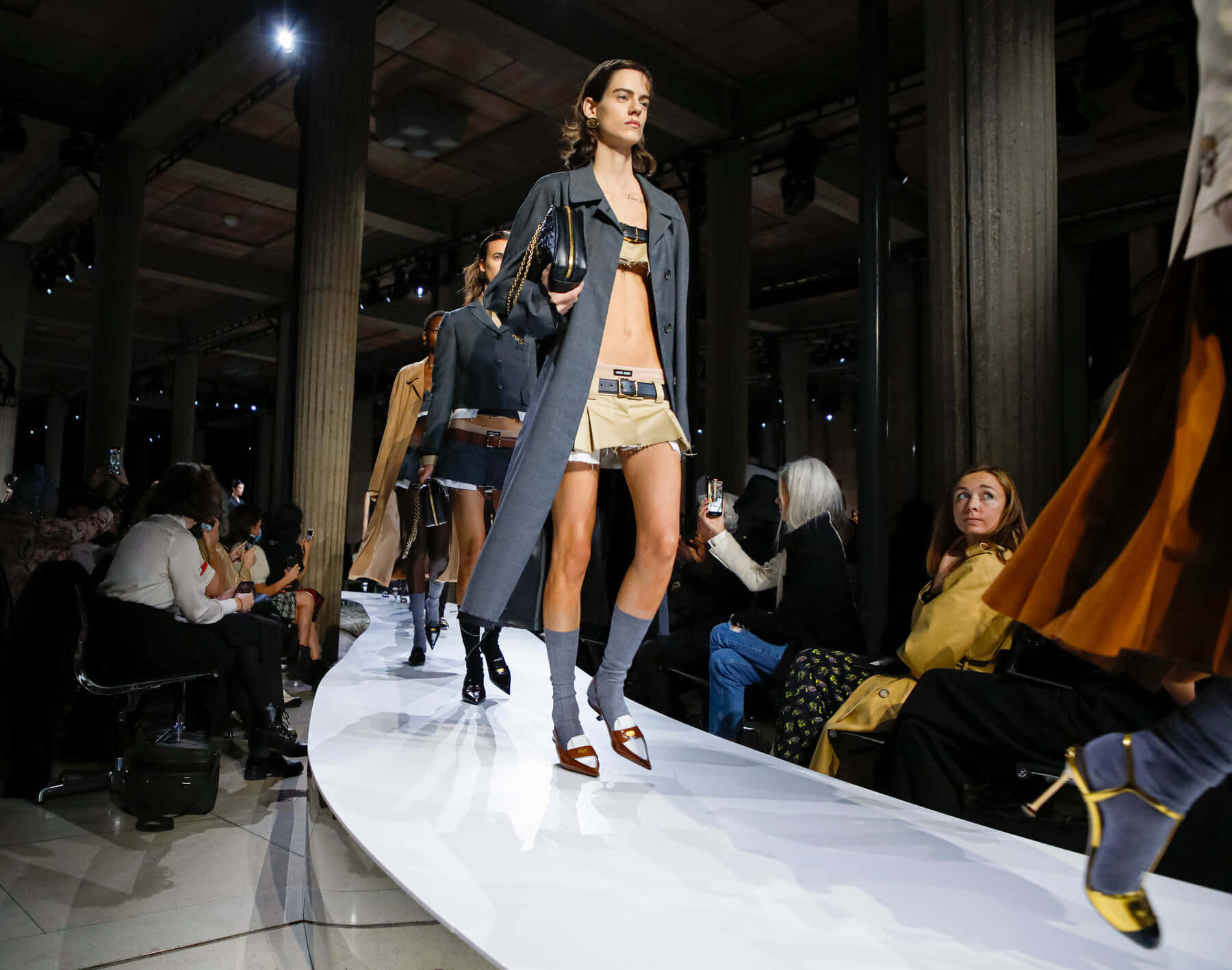 Runway 桌布 壁紙 — 一位模特兒自信地走在工業場地的彎曲白色天橋上，觀眾捕捉這一刻。