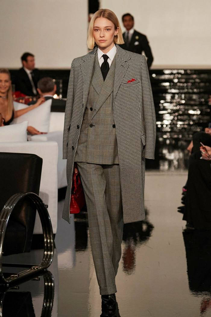 ralph lauren 桌布 壁紙 — 一位模特兒自信地走在閃亮的伸展台上，身穿千鳥格大衣和配套西裝，手持紅色手提包。
