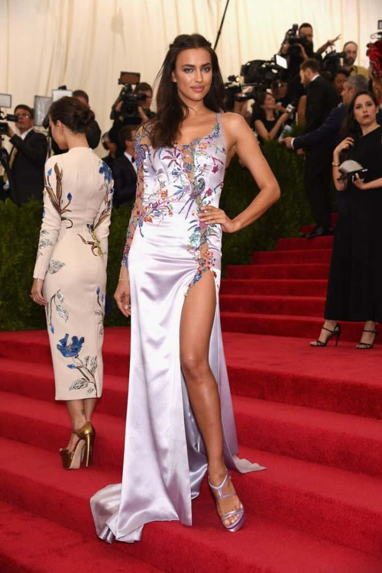 Met Gala 桌布 壁紙 — 一位模特兒身穿帶有花卉刺繡的白色緞面禮服，在華麗活動的紅地毯上自信地擺姿勢。