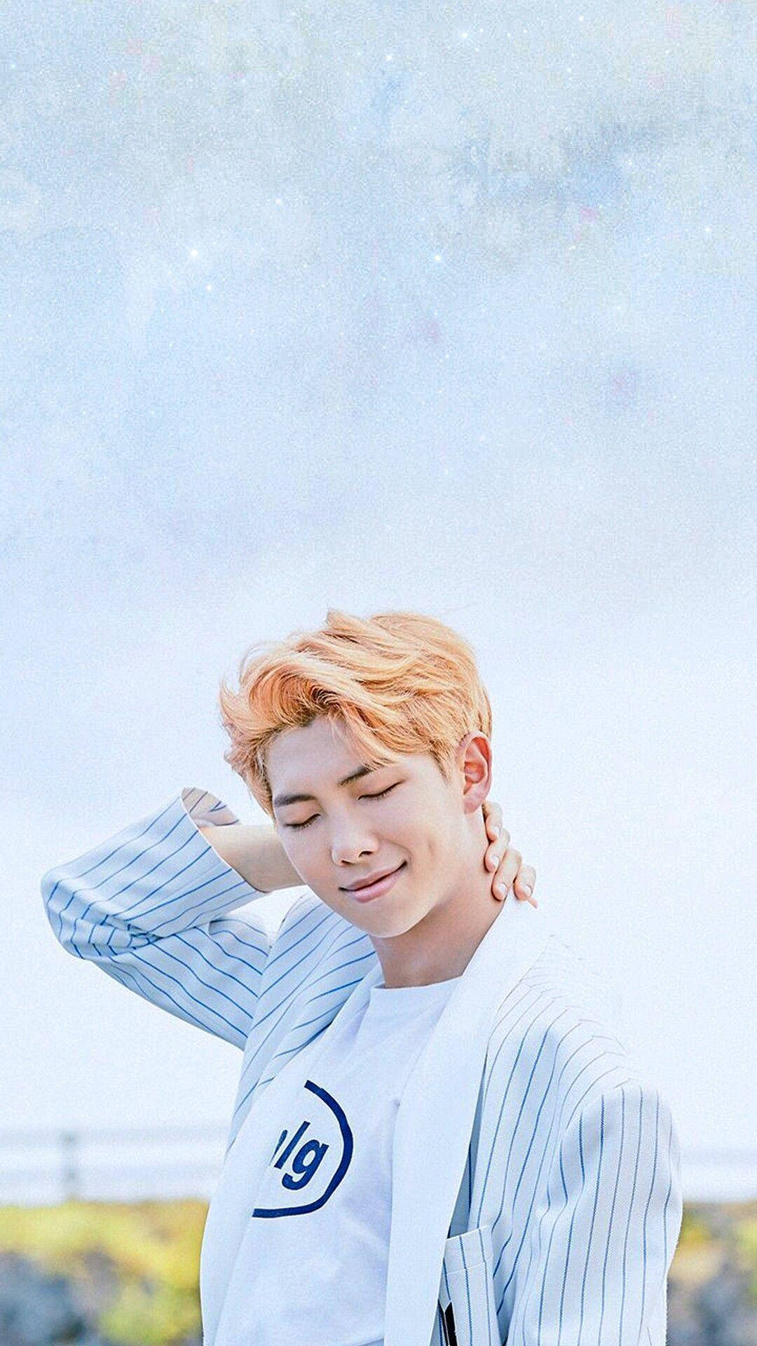 Cute Bts 桌布 壁紙 — 一位橙色頭髮的年輕男子在柔和藍天與閃爍光效的背景下，一邊調整他的條紋外套，一邊溫柔微笑。