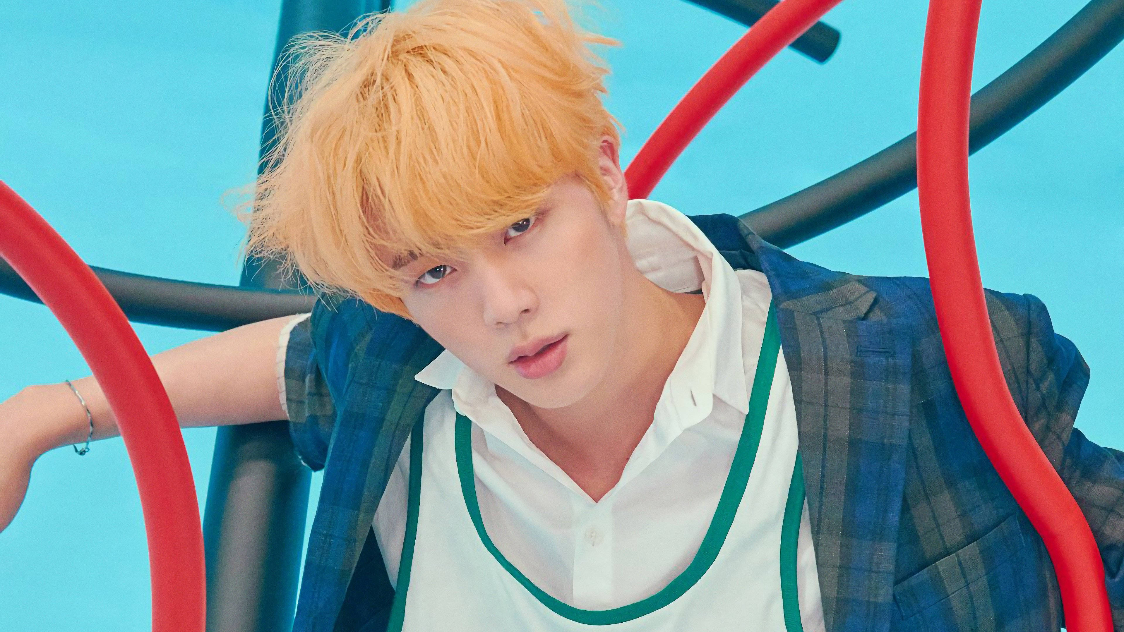 kim seok jin 桌布 壁紙 — 一位橙色頭髮的年輕男子靠在紅色和黑色的管子上，背景是明亮的藍色。