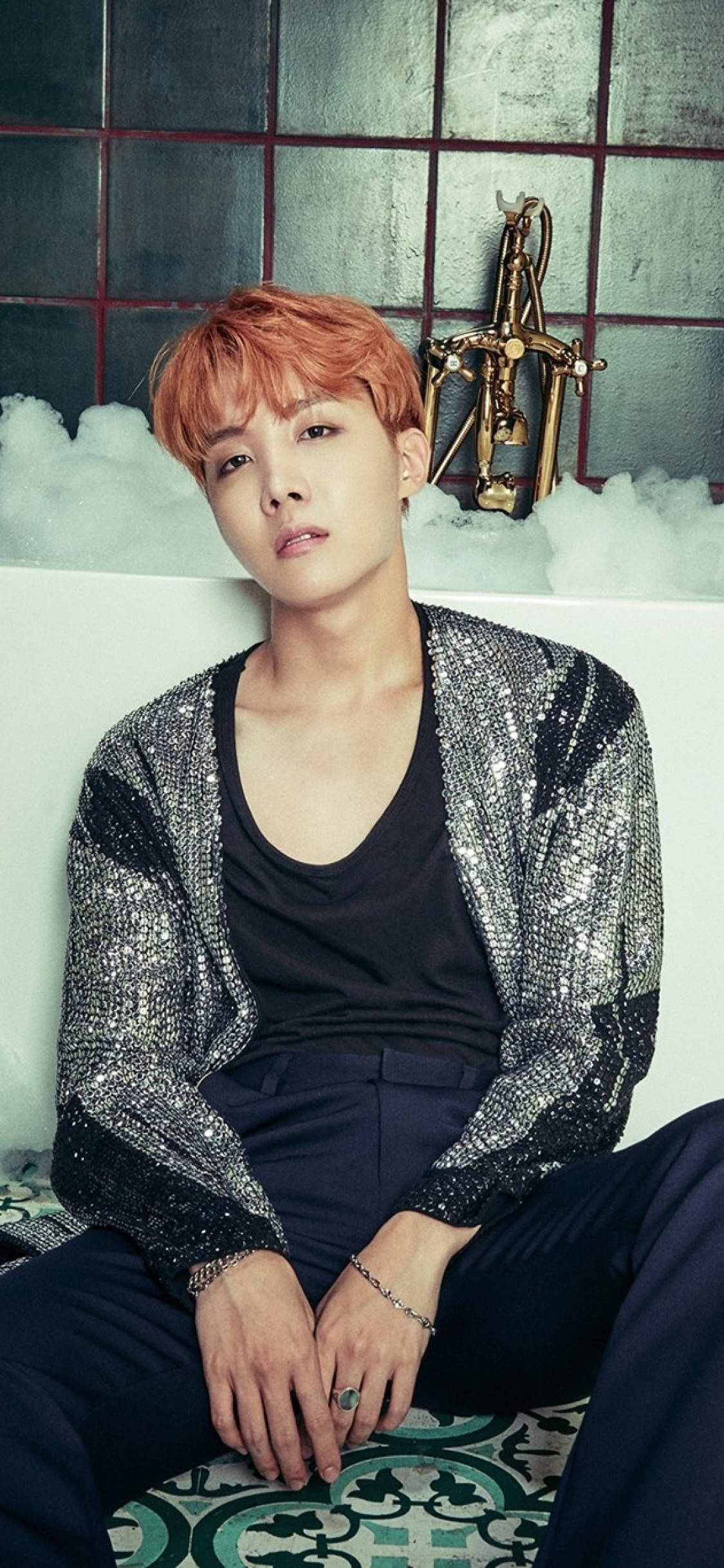 jhope 桌布 壁紙 — 一位橙髮年輕男子坐在充滿白色泡沫的浴缸中，身穿閃亮銀色外套，背景是瓷磚牆，牆上有金色劍裝飾。