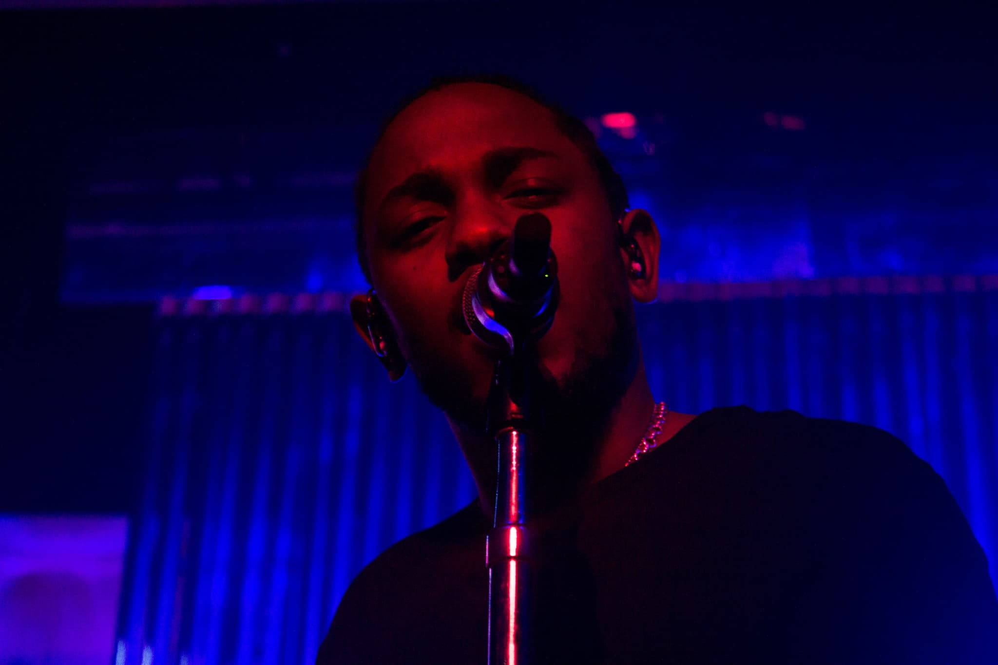 Kendrick 桌布 壁紙 — 一位歌手在強烈的紅色和藍色舞台燈光下表演，麥克風靠近他的嘴。