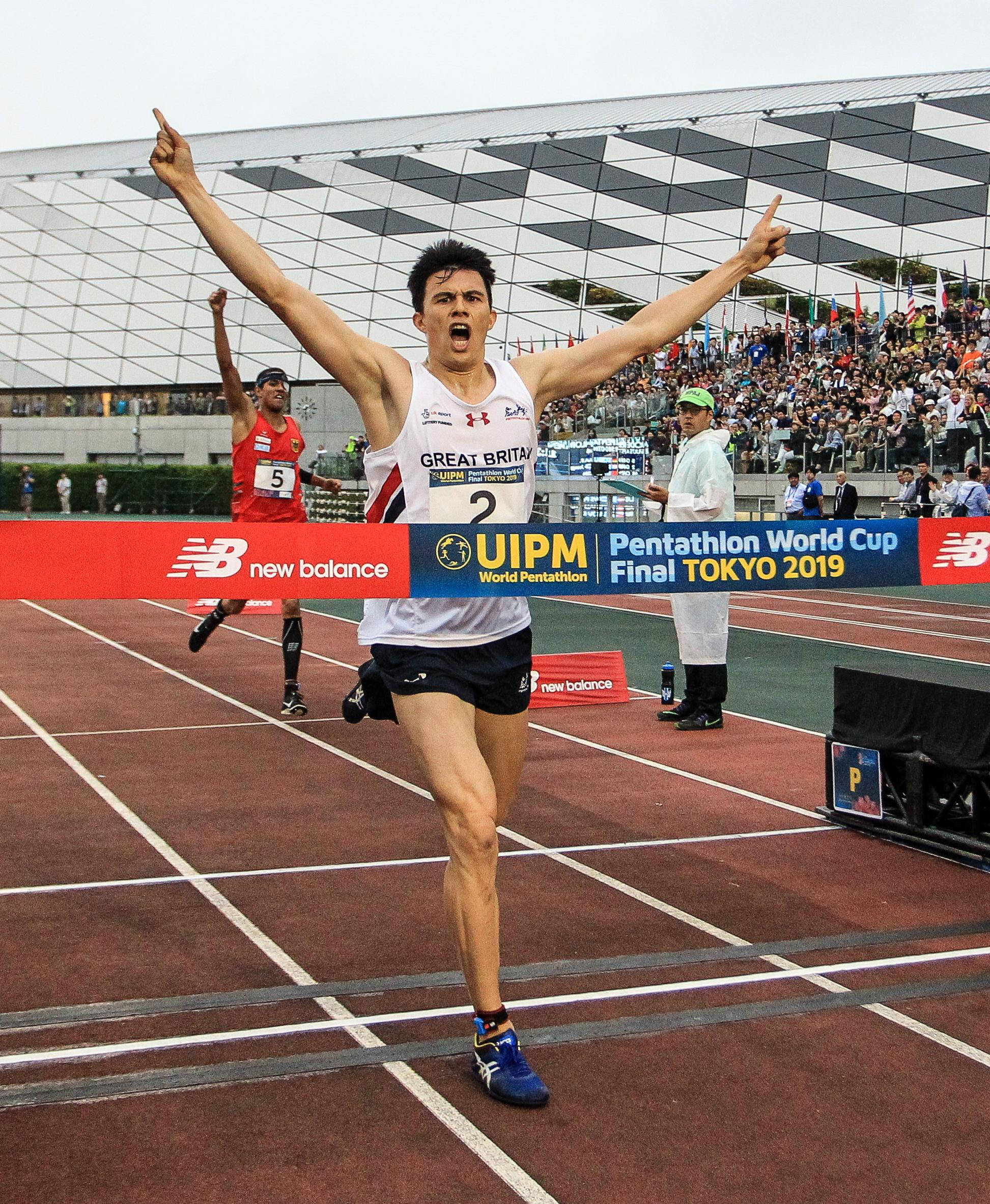 運動 桌布 壁紙 — 一位歡欣鼓舞的英國現代五項運動員在東京2019世界盃中高舉雙臂衝過終點線。