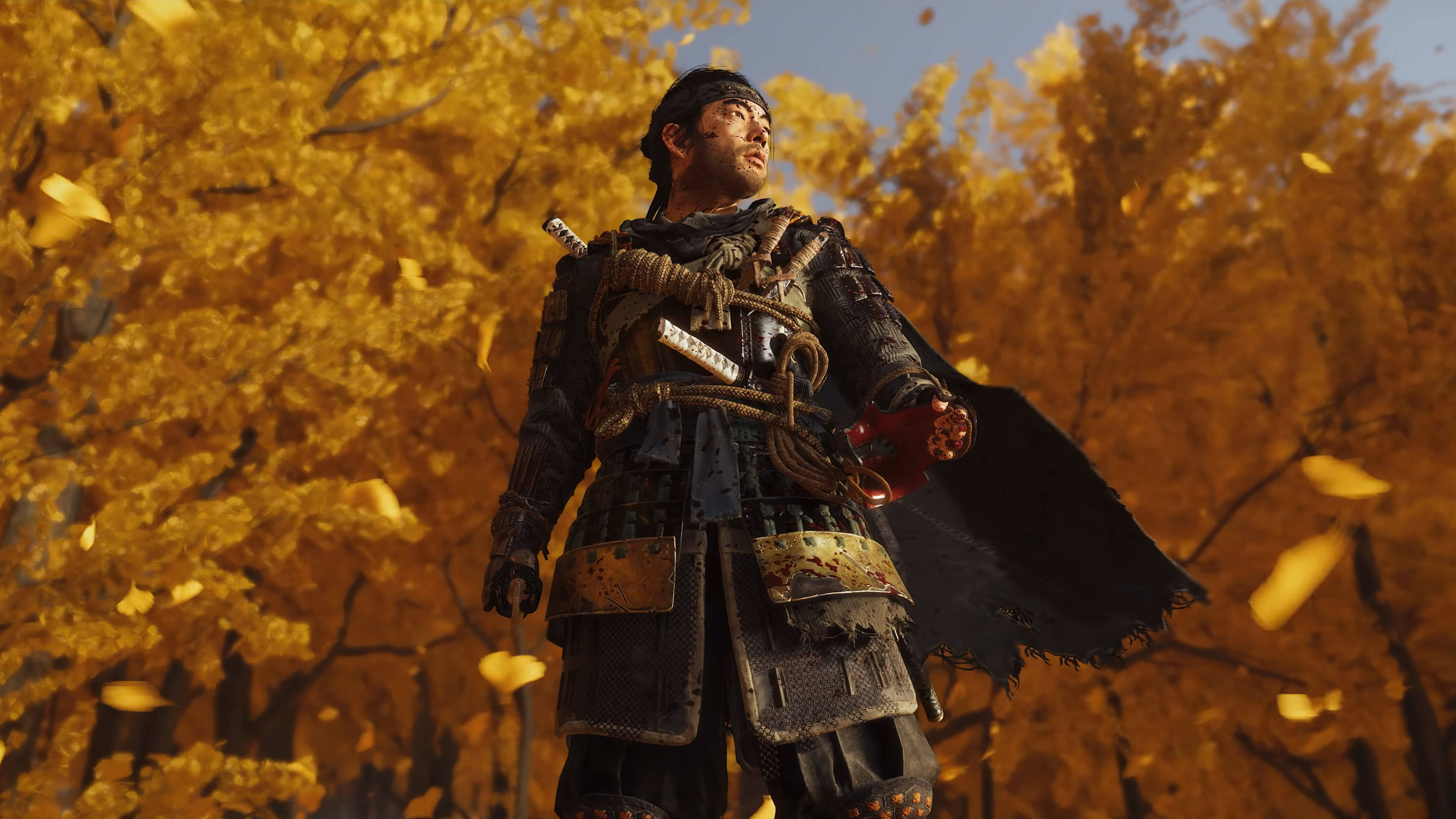 Ghost Of Tsushima 桌布 壁紙 — 一位武士戰士站在秋日晴朗藍天下，金色落葉紛飛之中。