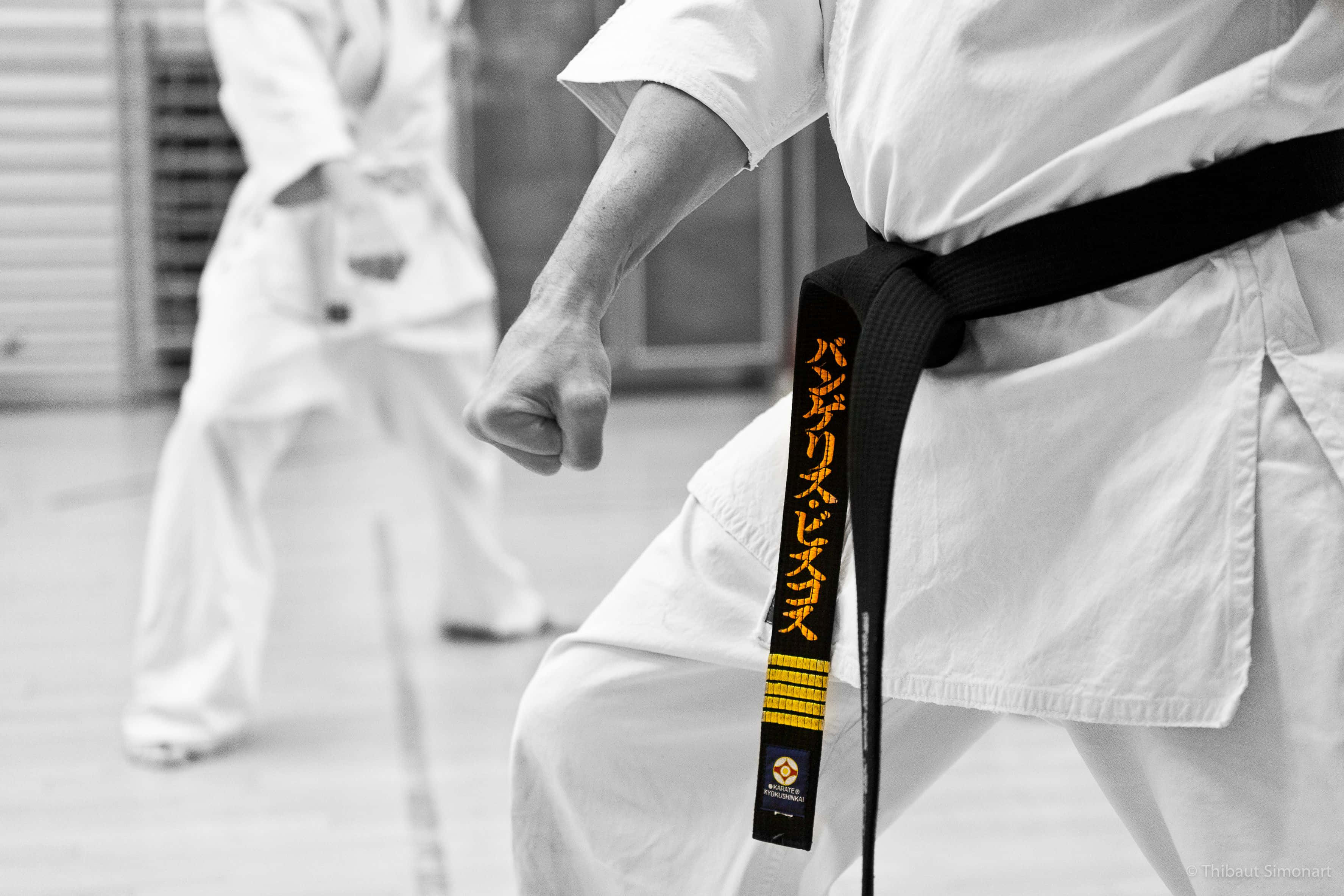 Martial Arts Uniform 桌布 壁紙 — 一位武術家在訓練期間握緊拳頭和帶有金色漢字的黑色腰帶的黑白特寫。