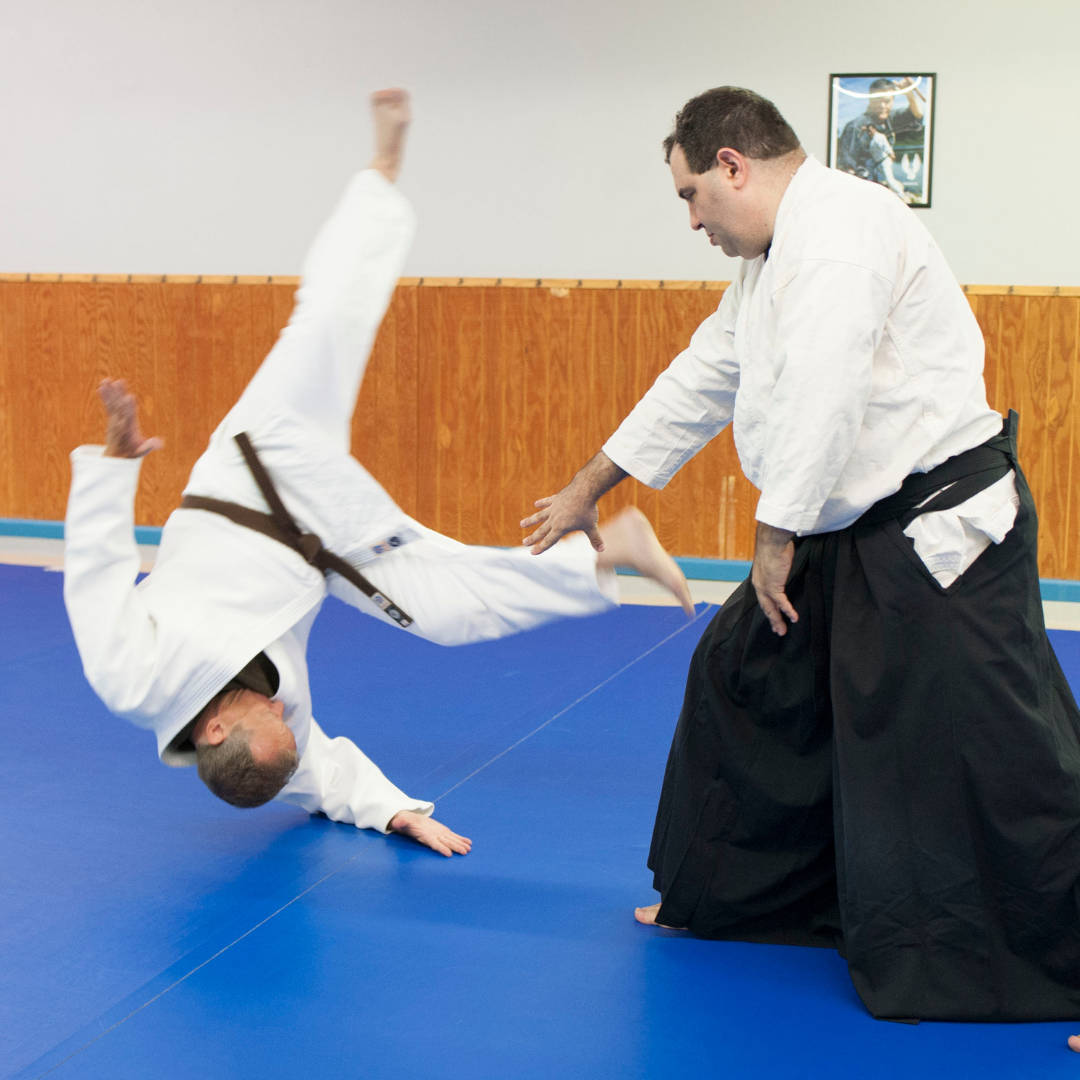 martial arts 桌布 壁紙 — 一位武術家在道場的藍色墊子上進行合氣道訓練時執行一個動態投擲。