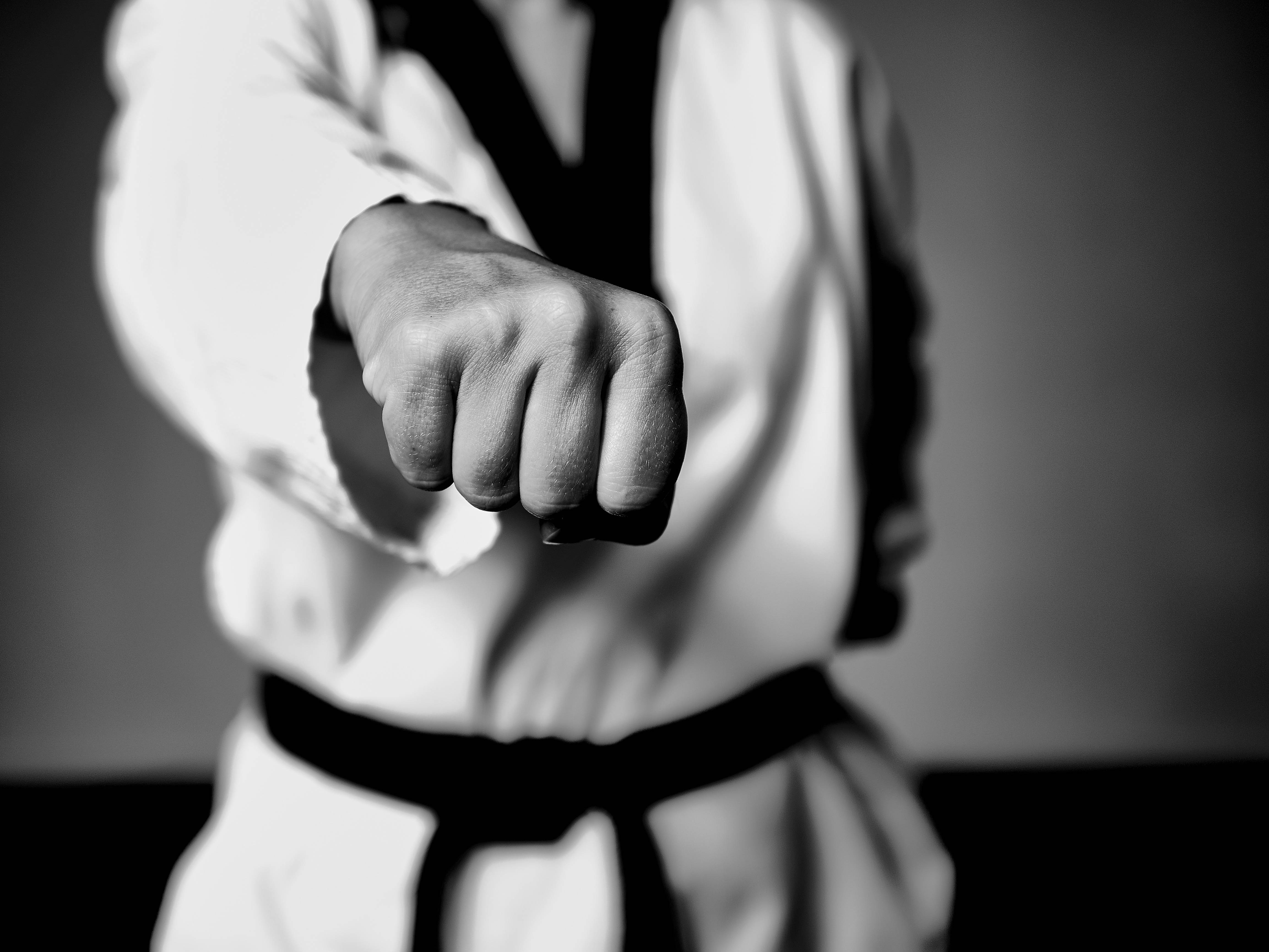 黑白 桌布 壁紙 — 一位武術家身穿白色道服、繫著黑色腰帶，握緊拳頭向前猛衝的黑白特寫。