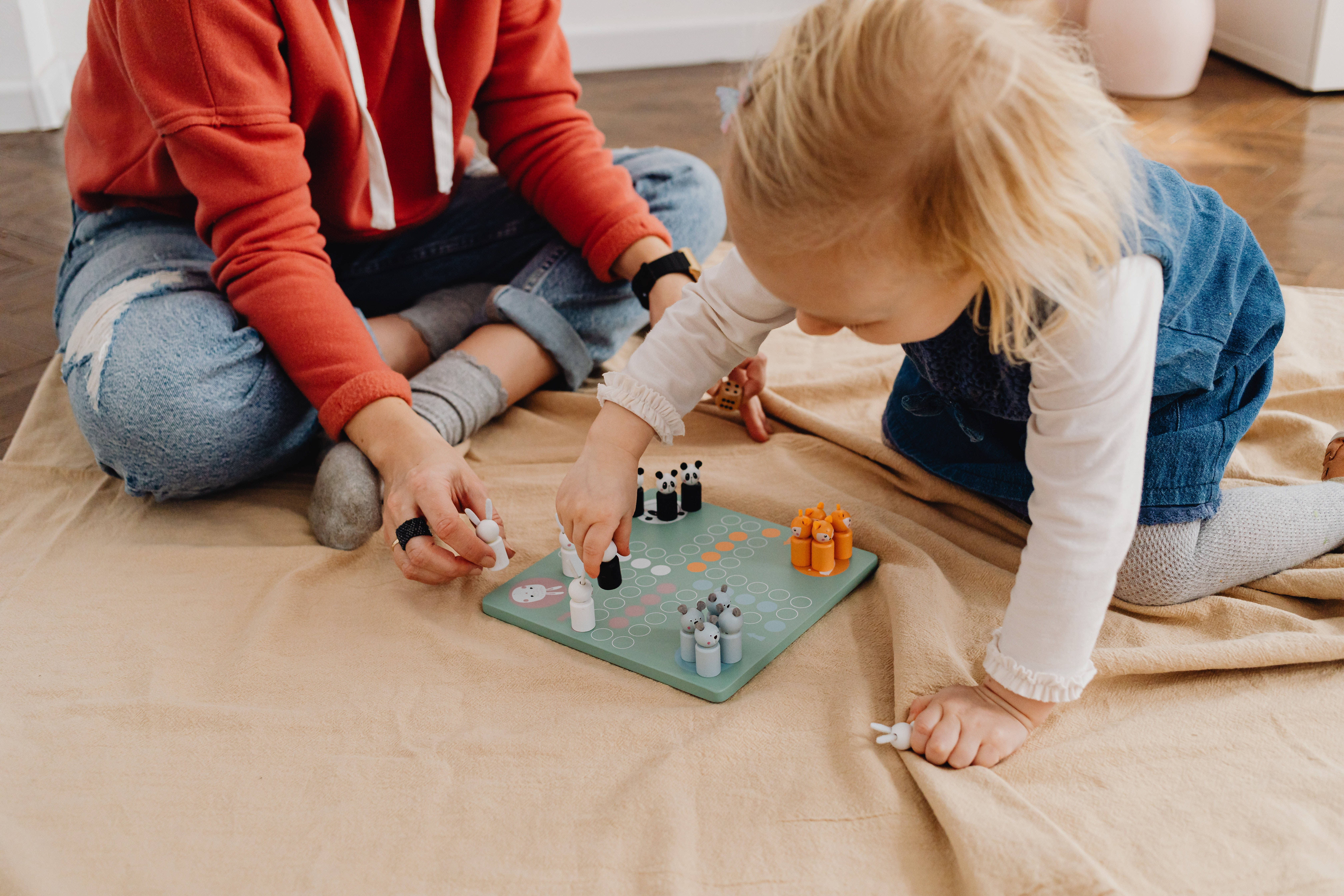 桌布 壁紙 — 一位母親和一個幼兒在室內的米色毯子上一起玩色彩繽紛的棋盤遊戲。