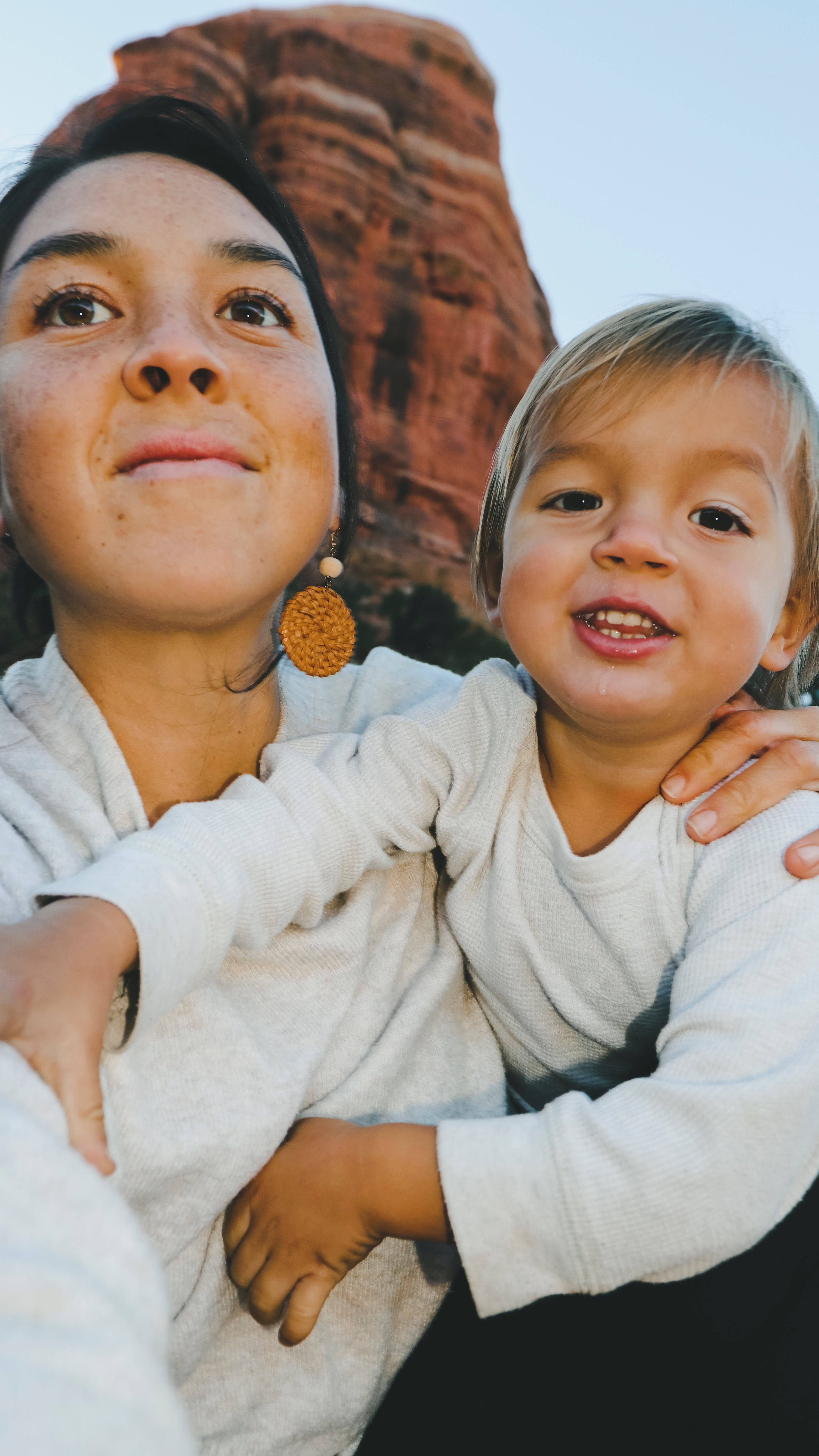 Family 桌布 壁紙 — 一位母親和幼兒在晴朗的天空下，以紅色岩層為背景，溫暖地微笑擁抱。