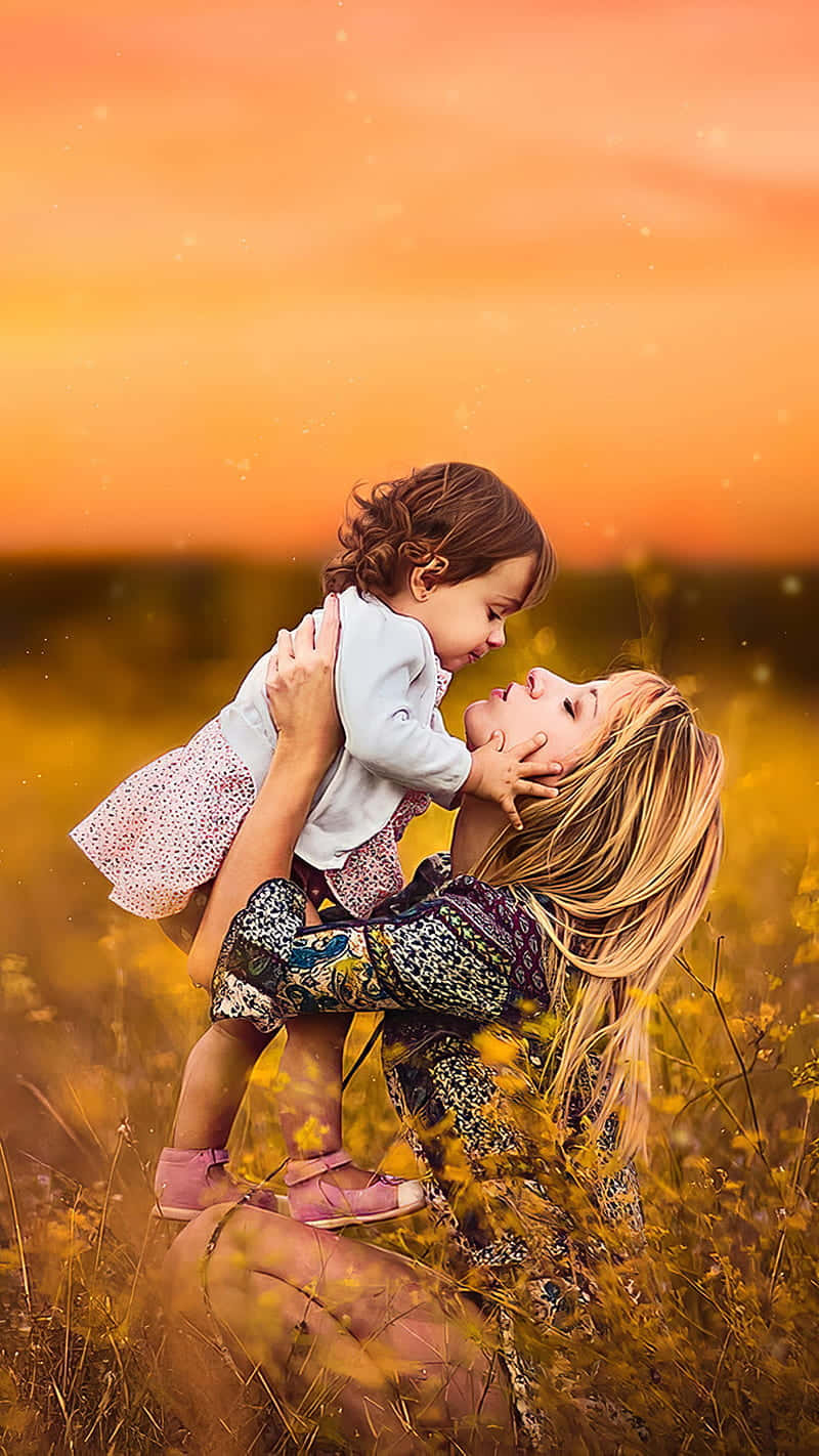 Mother Love 桌布 壁紙 — 一位母親在金色田野中舉起女兒，她們在溫暖的日落天空下深情地凝視著對方。