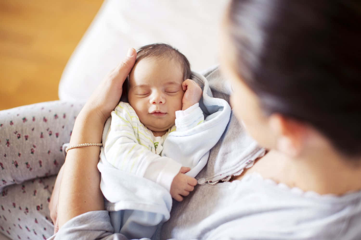 Newborn Baby 桌布 壁紙 — 一位母親輕輕地抱著她熟睡的新生嬰兒，用柔軟的毯子包裹著，放在有圖案的沙發上。
