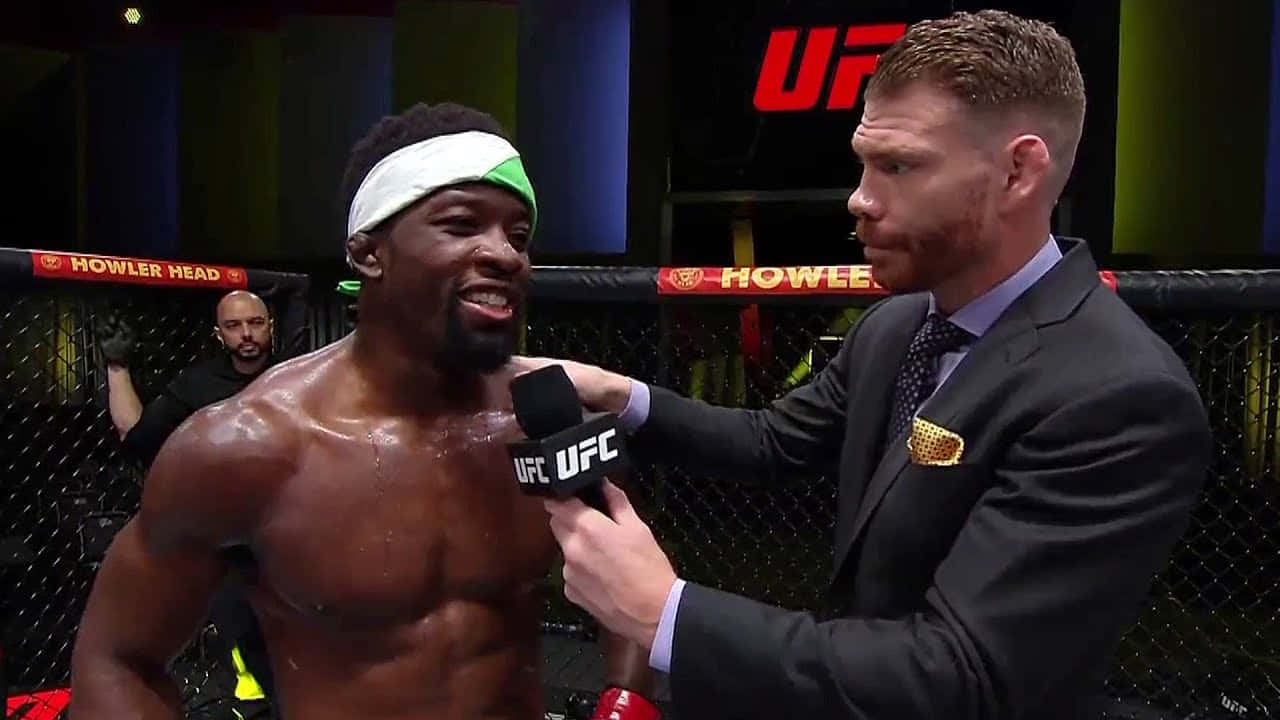 MMA 桌布 壁紙 — 一位汗流浹背的UFC拳手，戴著白色和綠色的頭帶，在八角籠內接受身穿西裝的採訪者訪問時露出燦爛的笑容。