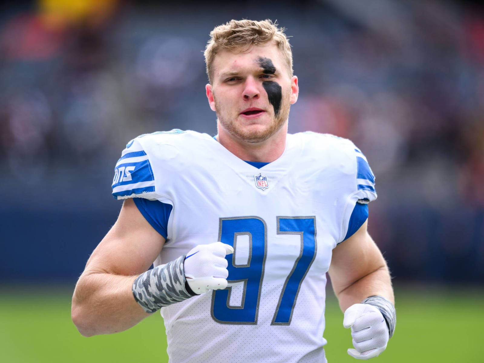 Detroit Lions 桌布 壁紙 — 一位決心堅定的NFL球員，身穿白色和藍色球衣，號碼97，帶著黑色眼部塗料，在陽光明媚的場地上衝刺。