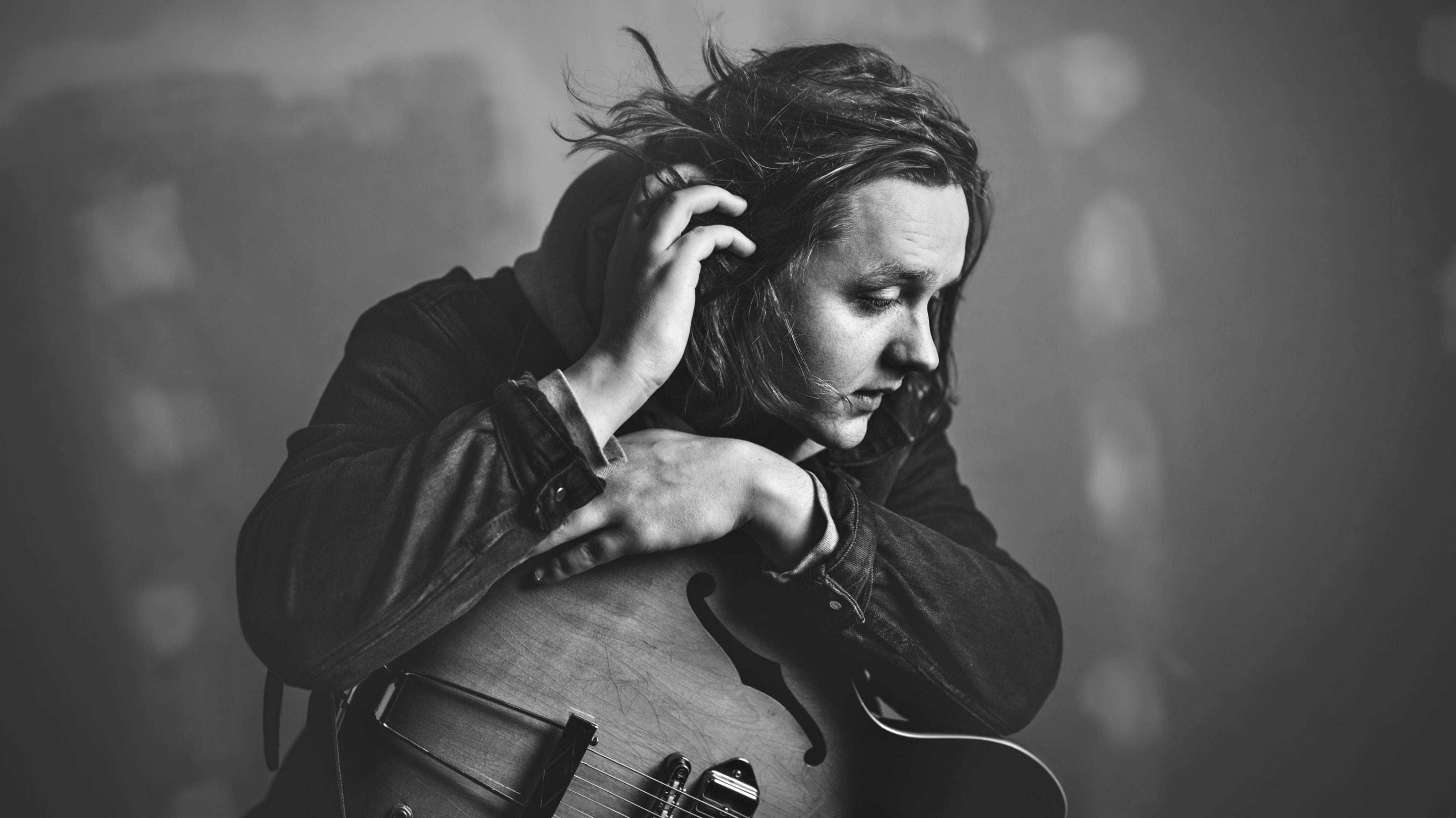 Lewis Capaldi 桌布 壁紙 — 一位沉思的音樂家懷抱著一把空心吉他，背景是柔和模糊的黑白畫面。