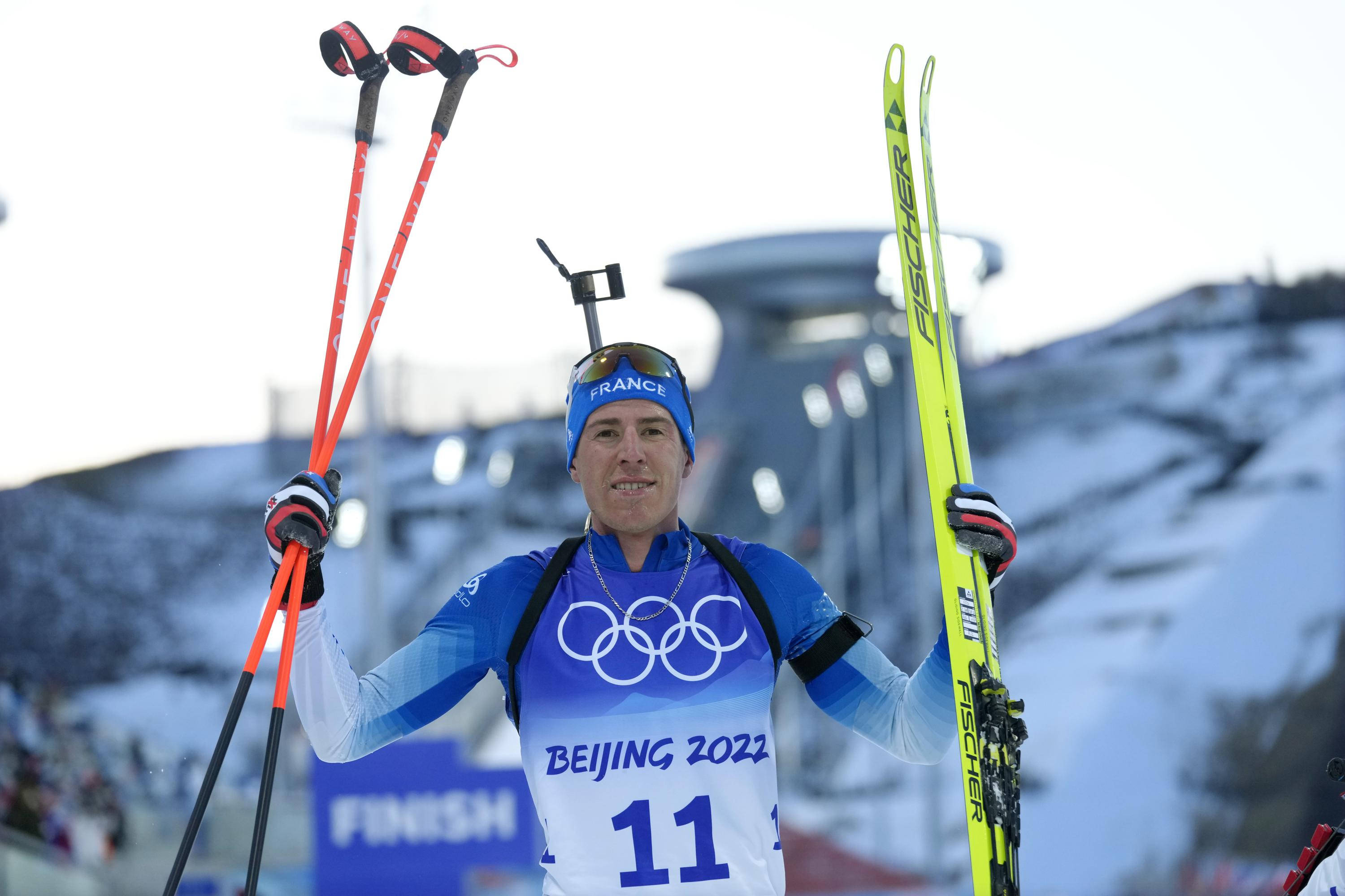 運動 桌布 壁紙 — 一位法國跳台滑雪運動員在北京2022年冬奧會上慶祝勝利，手持滑雪板和滑雪杖，背景是雪山。