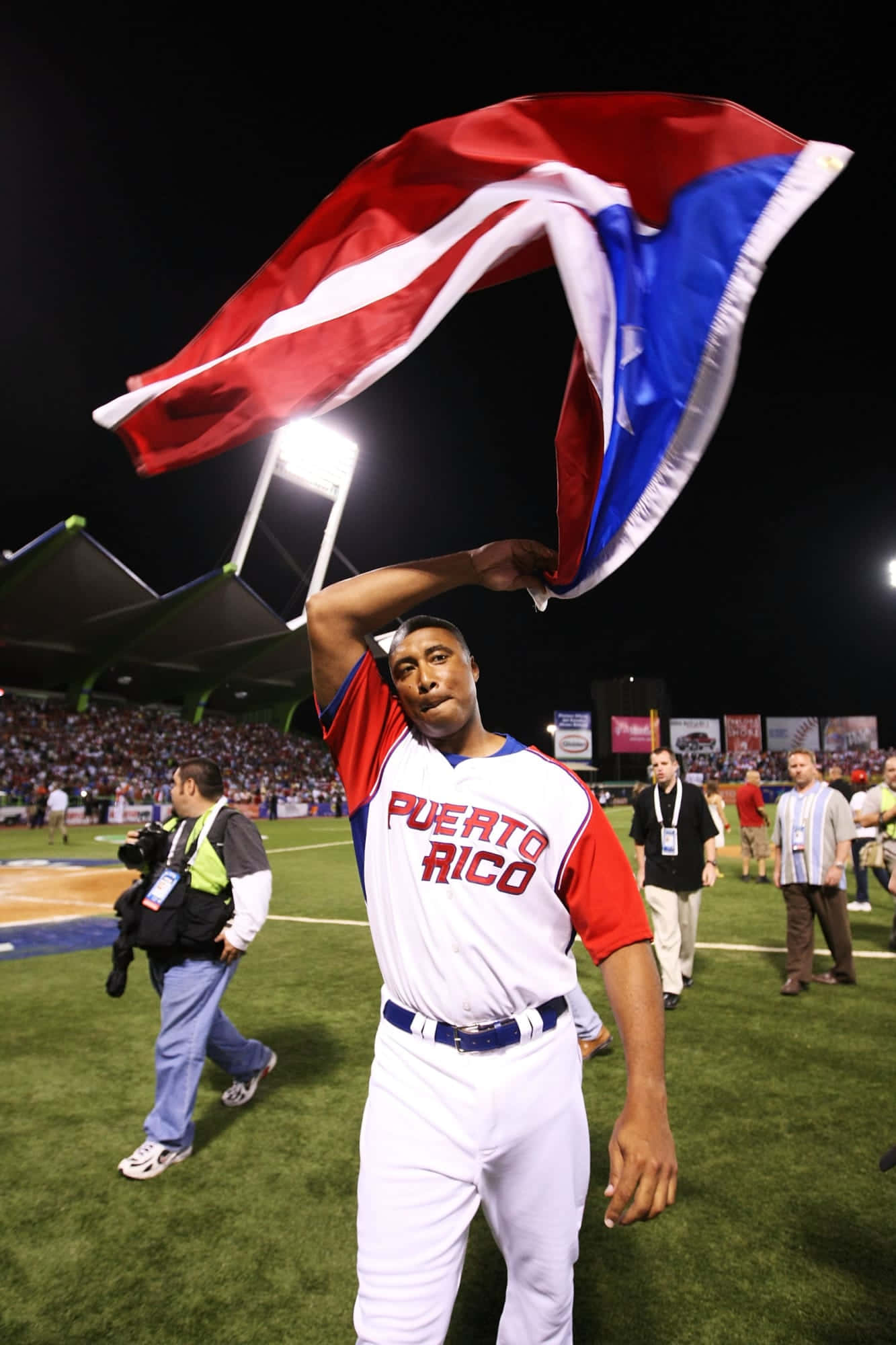 Puerto Rican 桌布 壁紙 — 一位波多黎各棒球運動員在夜間比賽中，在體育場燈光下自豪地揮舞著他的旗幟。