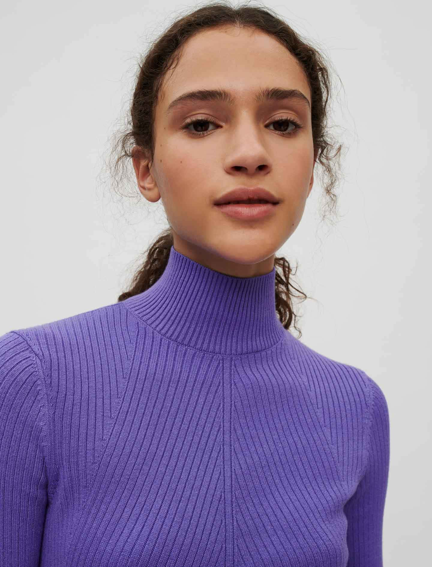 Purple Turtle-neck Sweater 桌布 壁紙 — 一位深色捲髮女性穿著紫色羅紋高領毛衣，背景為純白色。