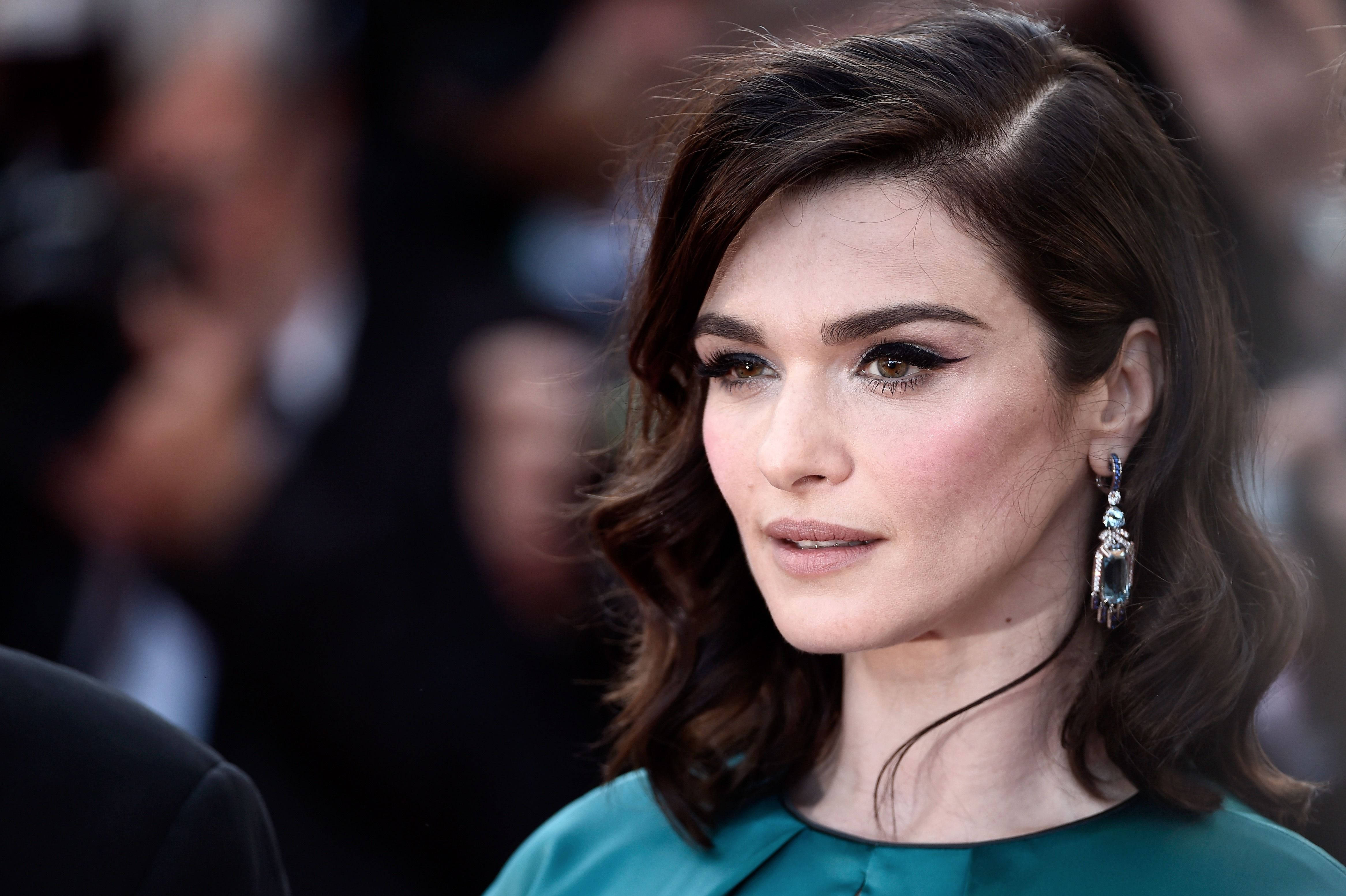 Rachel Weisz 桌布 壁紙 — 一位深色波浪髮、身穿藍綠色連衣裙的女性在紅地毯活動中的特寫肖像。