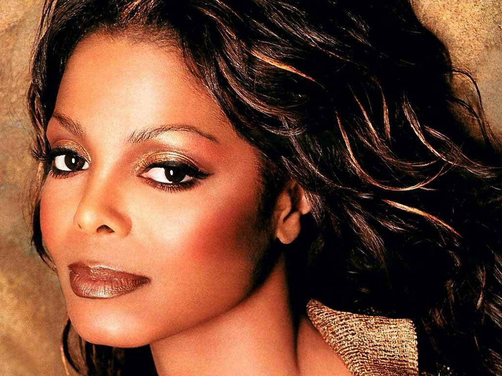 janet jackson 桌布 壁紙 — 一位深色波浪髮、閃爍金色化妝的女性特寫肖像，背景為溫暖的紋理背景。