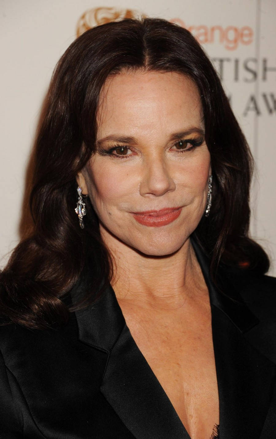 Celebrity 桌布 壁紙 — 一位深色波浪髮女性在頒獎活動中穿著黑色西裝外套和閃亮耳環的特寫肖像。