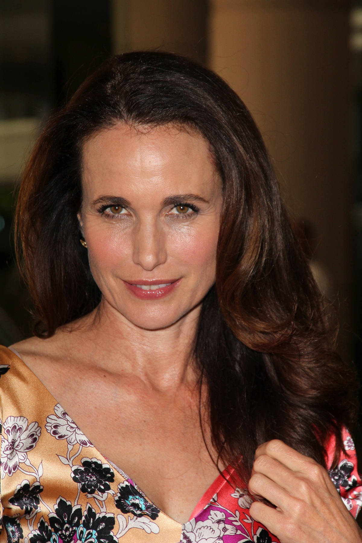andie macdowell 桌布 壁紙 — 一位深色波浪髮女性的特寫肖像，身穿金色和紅色調的花卉圖案上衣。