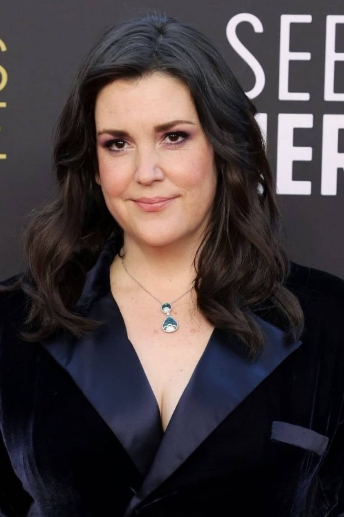Celebrity 桌布 壁紙 — 一位深色波浪髮的女性在正式活動中穿著黑色天鵝絨西裝外套和一條獨特的吊墜項鍊。
