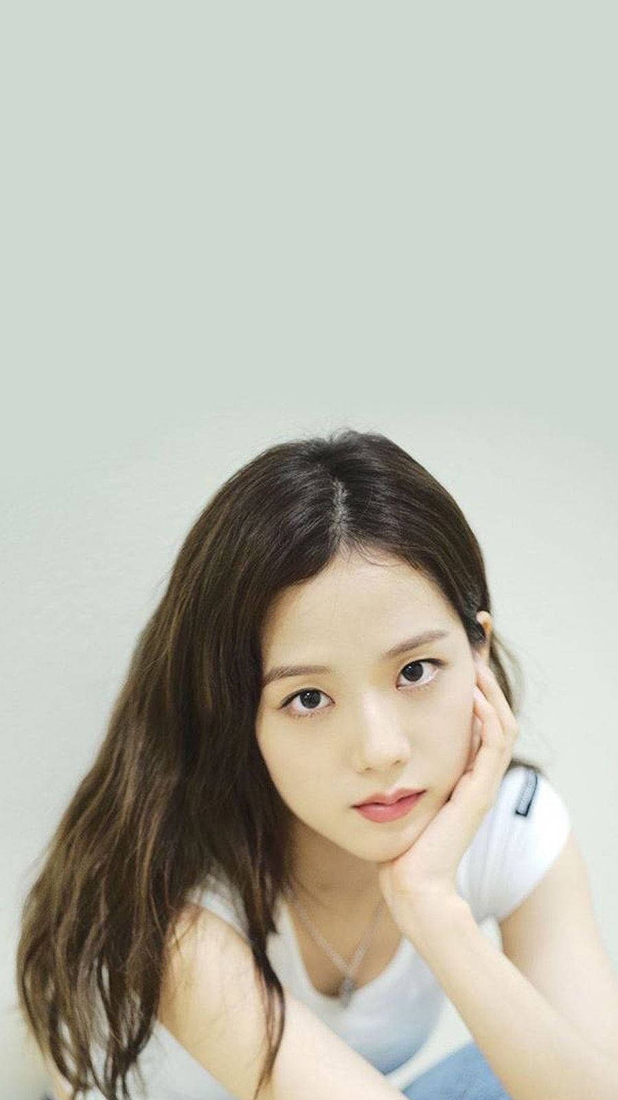 Jisoo Cute 桌布 壁紙 — 一位深色波浪髮的年輕女子，在柔和的淡綠色背景前，將下巴擱在手上。