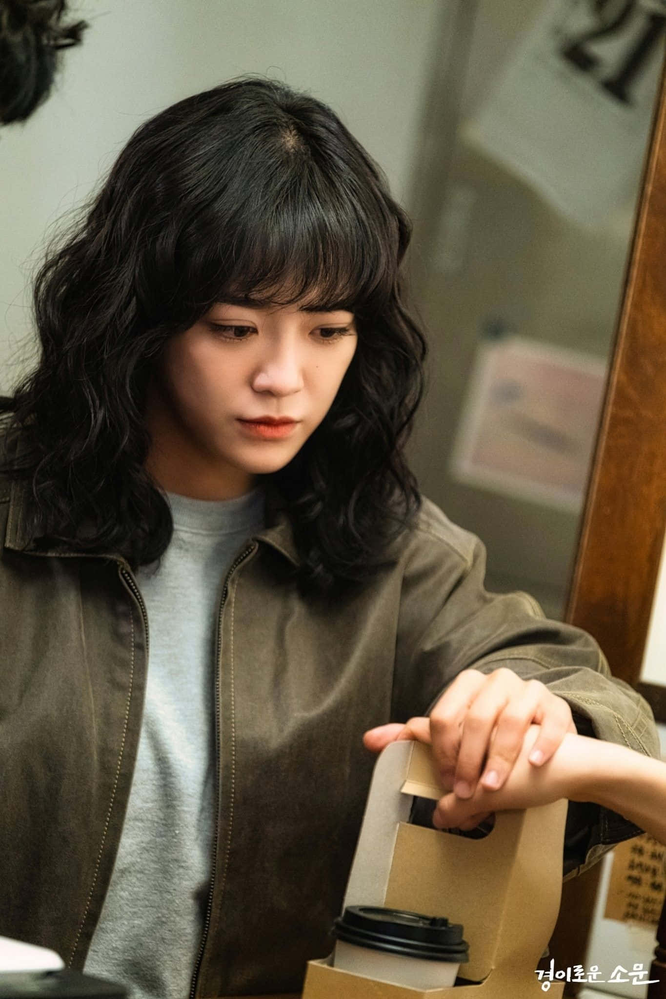 korean 桌布 壁紙 — 一位深色波浪髮的年輕女性穿著棕色外套，專注地拿著一個咖啡袋。