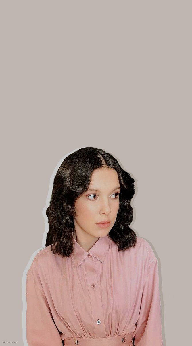 Millie 桌布 壁紙 — 一位深色波浪髮的年輕女性穿著粉紅色鈕扣襯衫，背景為純米色。