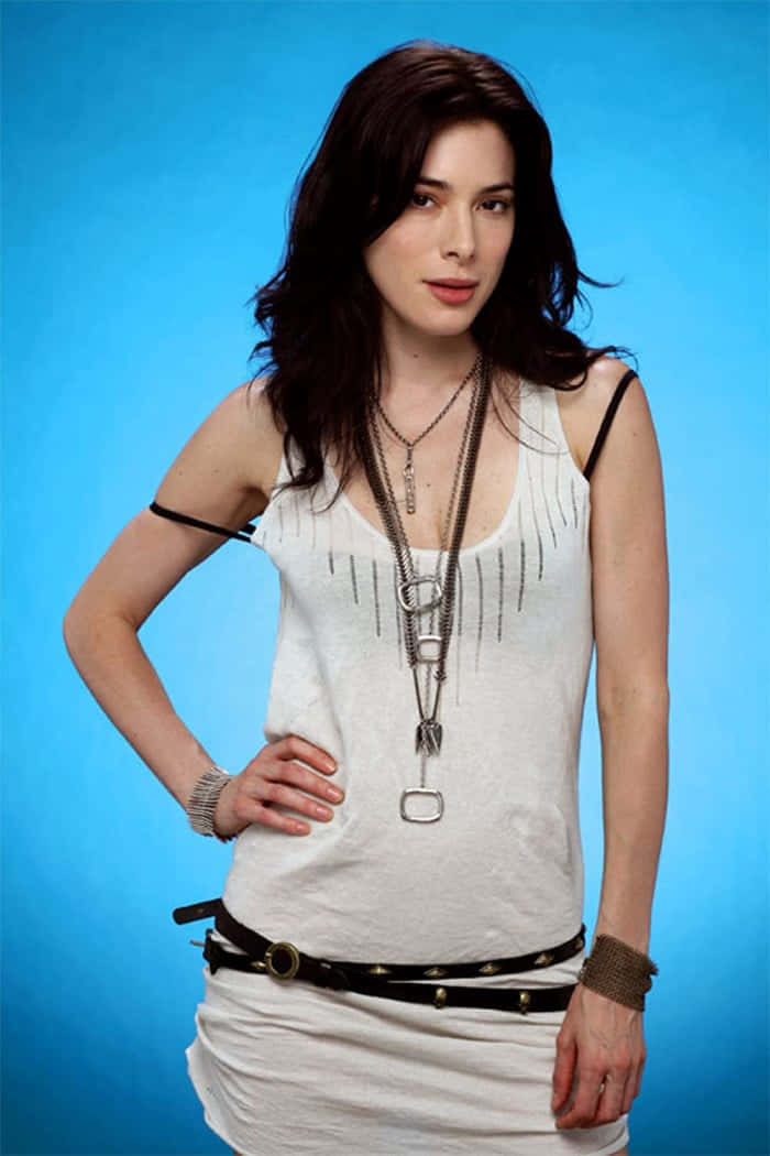 Jaime Murray 桌布 壁紙 — 一位深色頭髮、佩戴多層項鍊的女性在純藍色攝影棚背景前自信地擺姿勢。