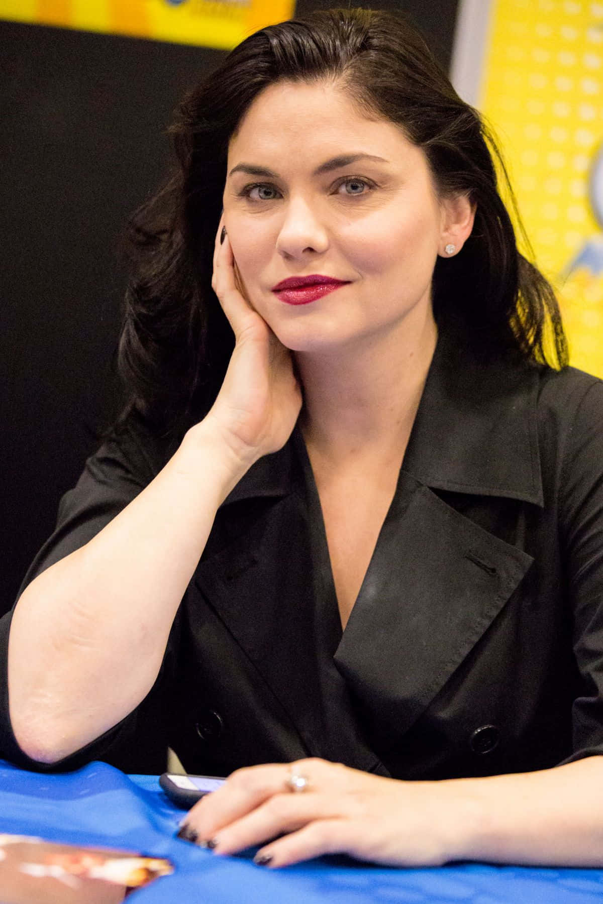 jodi lyn o'keefe 桌布 壁紙 — 一位深色頭髮、塗著紅色唇膏的女性，坐在藍色桌子旁，用手托著下巴。