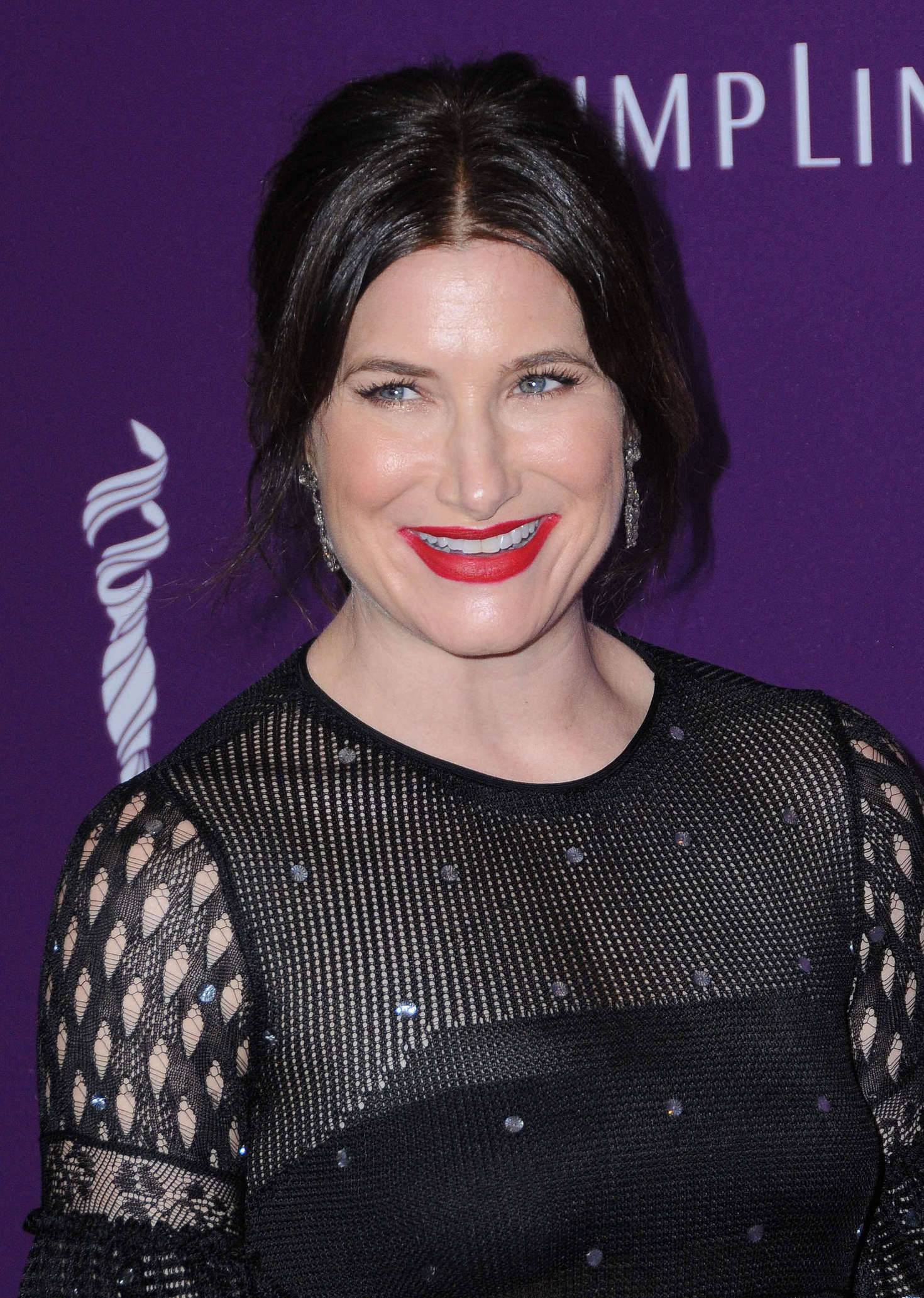Celebrity 桌布 壁紙 — 一位深色頭髮、塗著鮮紅色唇膏的女性，穿著黑色網狀連衣裙，在紫色背景前對著鏡頭微笑。
